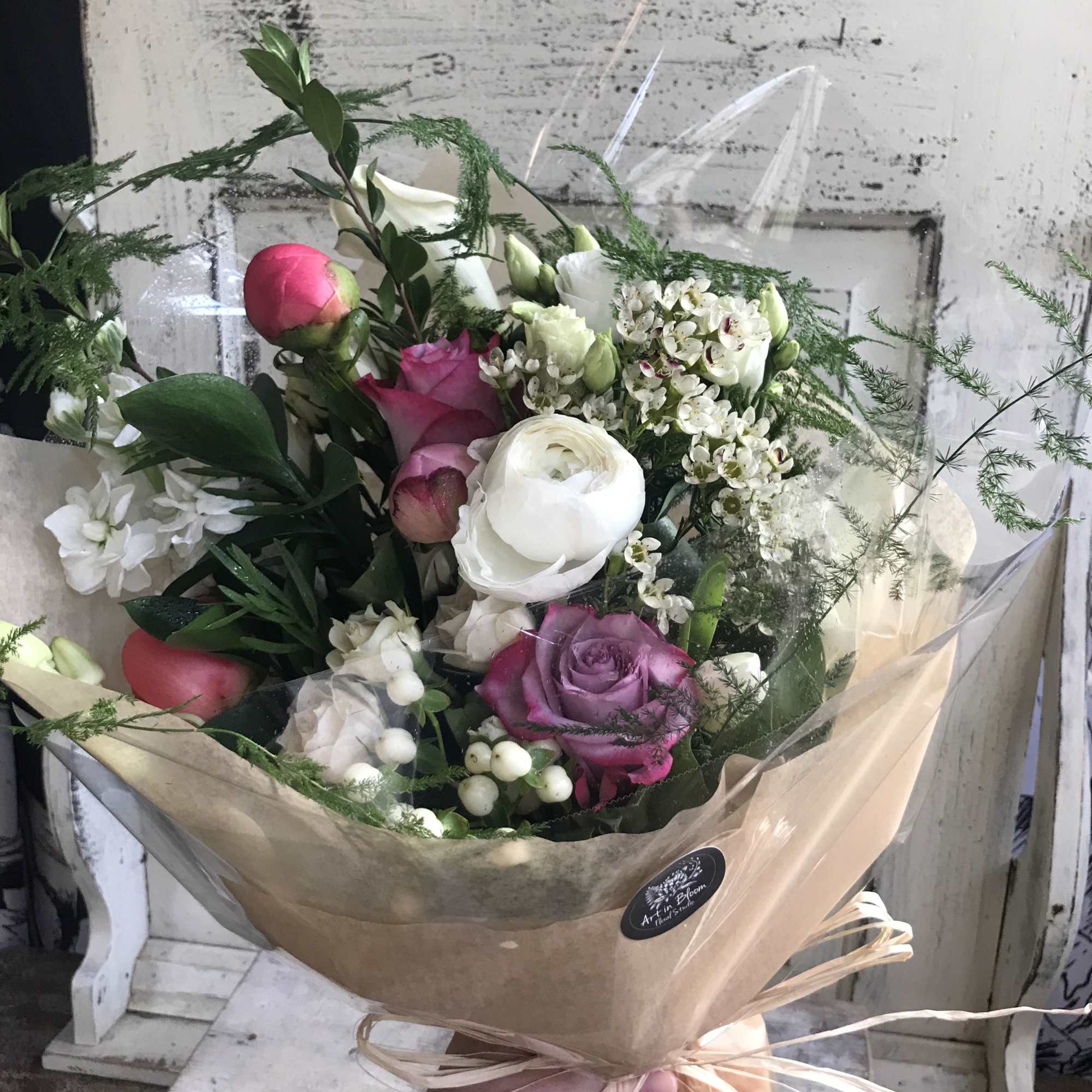 Hand-tied bouquet of pink, white, and purple flowers wrapped in tan paper