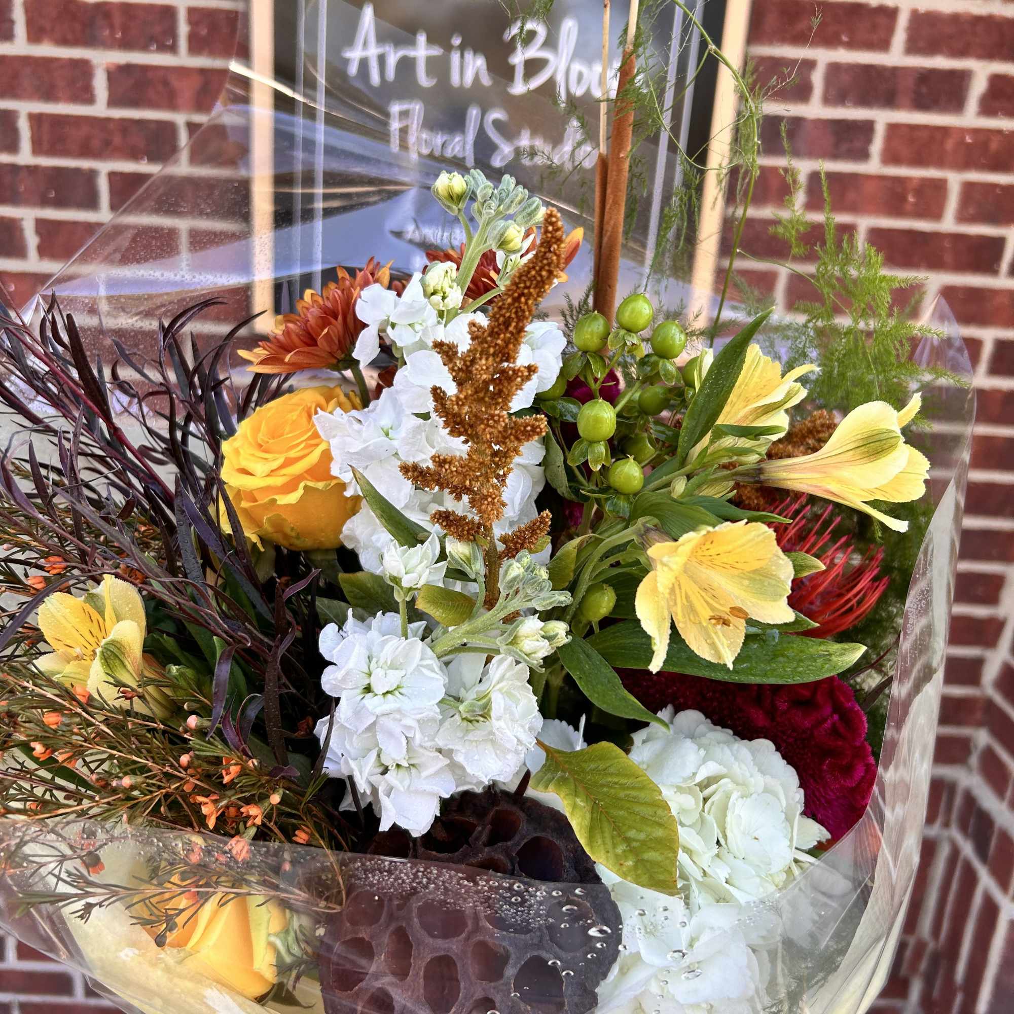 Mixed bouquet with yellow roses, white blooms, and orange flowers in clear wrap