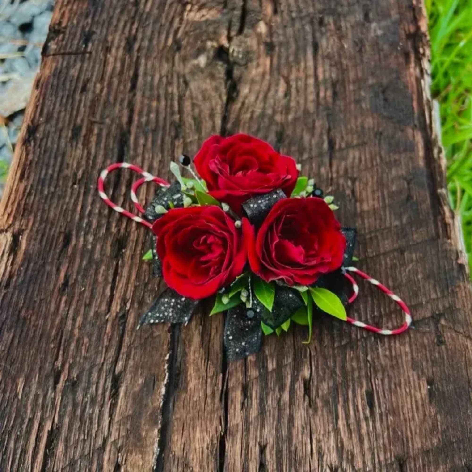 Three red roses with black ribbon accents on a rustic wood surface