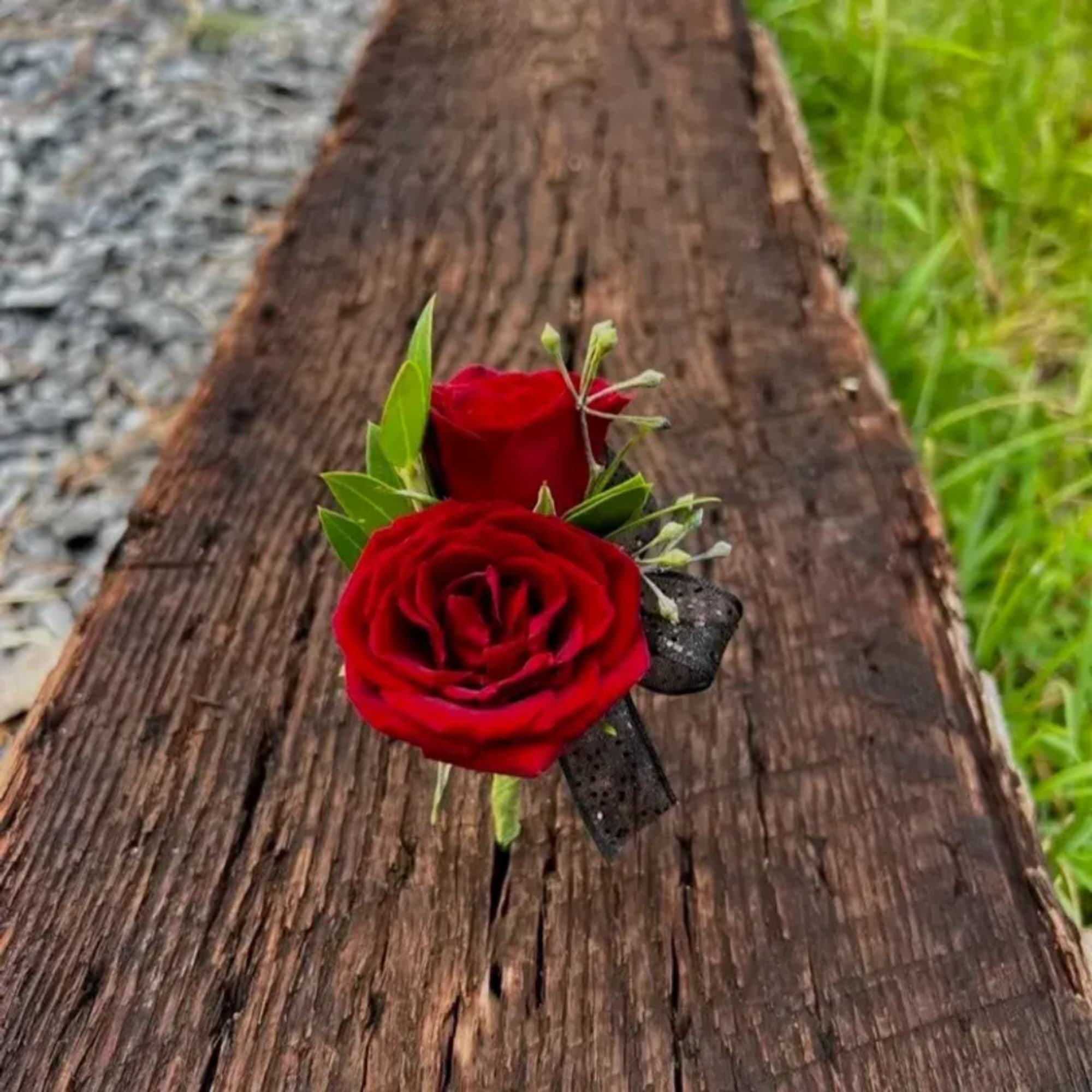 Two red rose boutonnieres with black ribbon on weathered wood