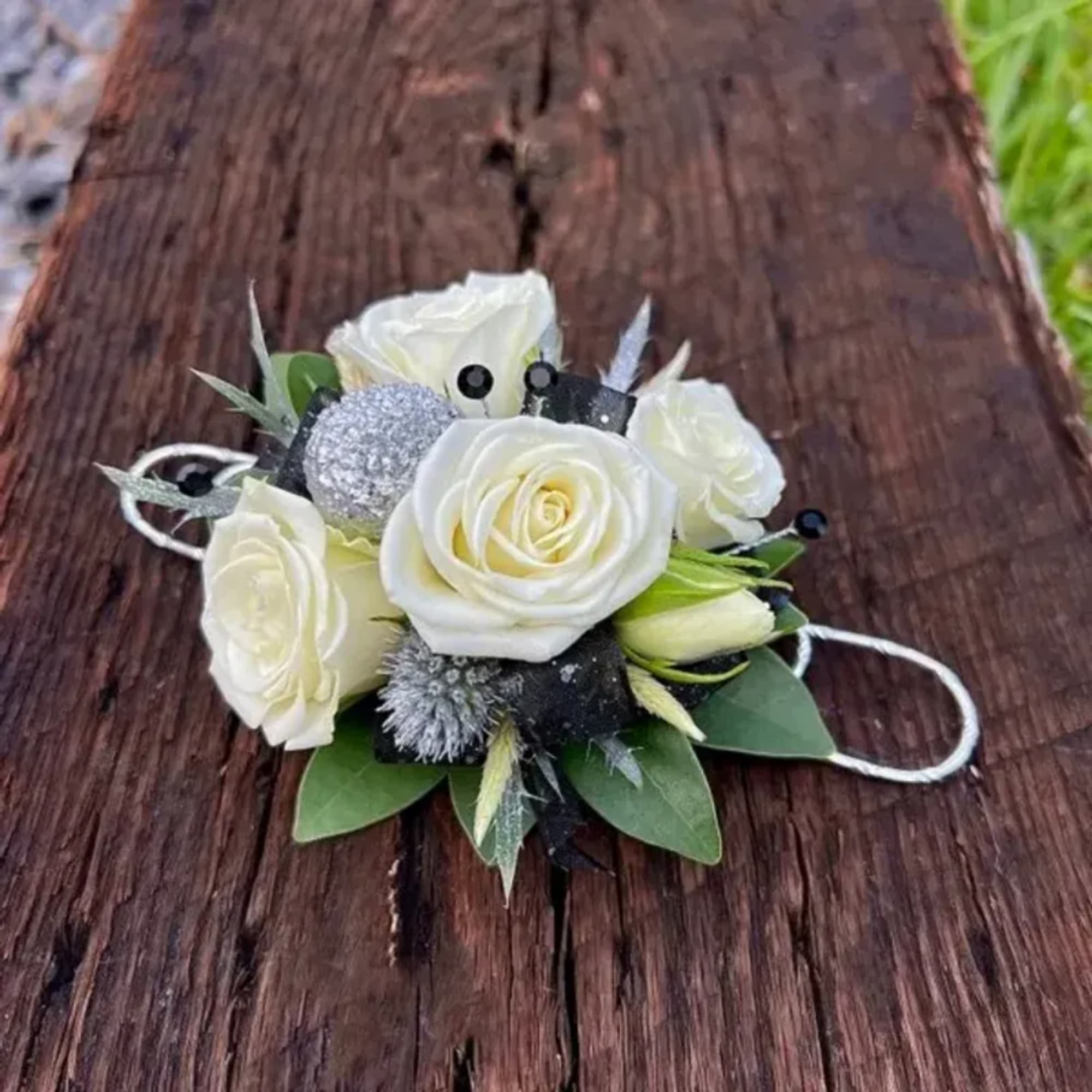 White rose corsage with silver accents on a wooden surface