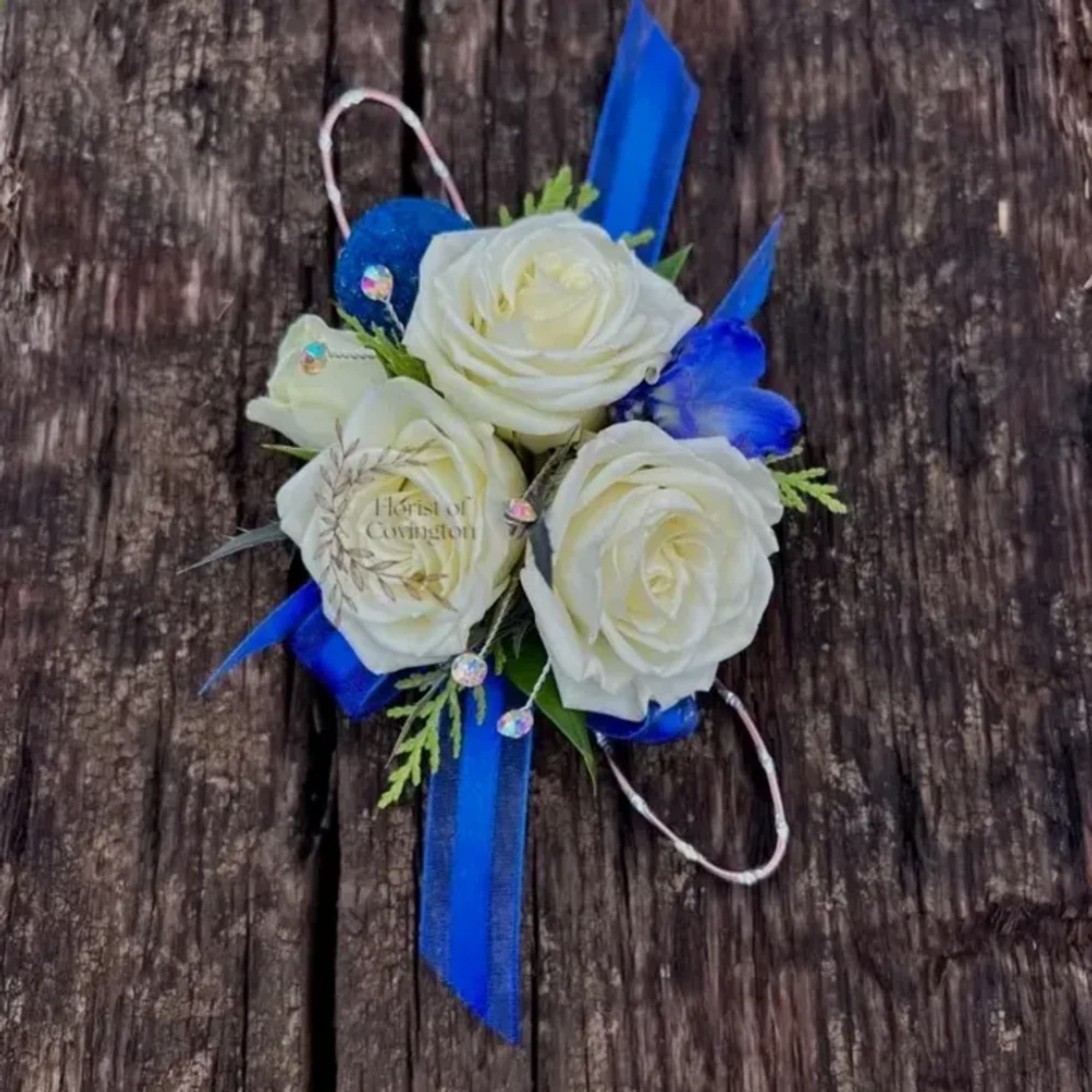 White rose corsage with blue ribbon and accents on a wooden surface