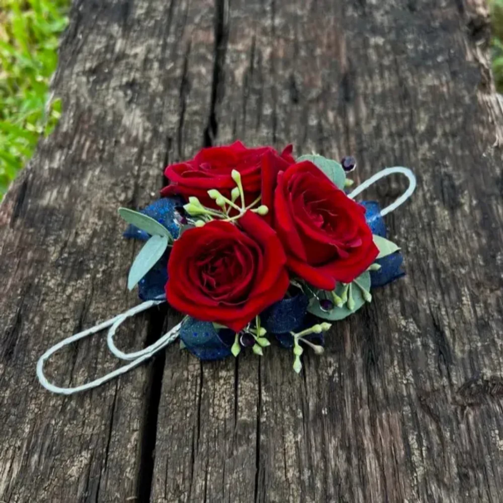 Small red rose corsage with blue accents on a wooden surface