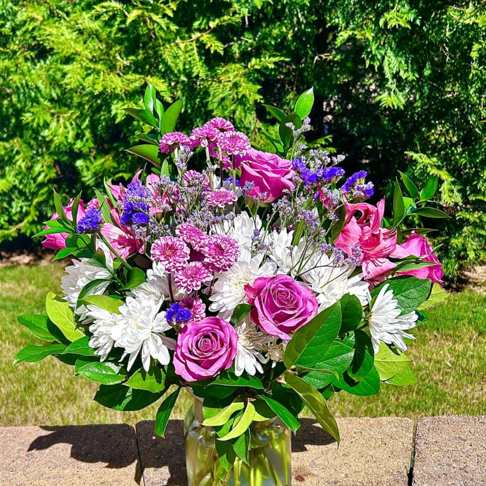 Pink roses and white daisies in a glass vase with purple filler flowers