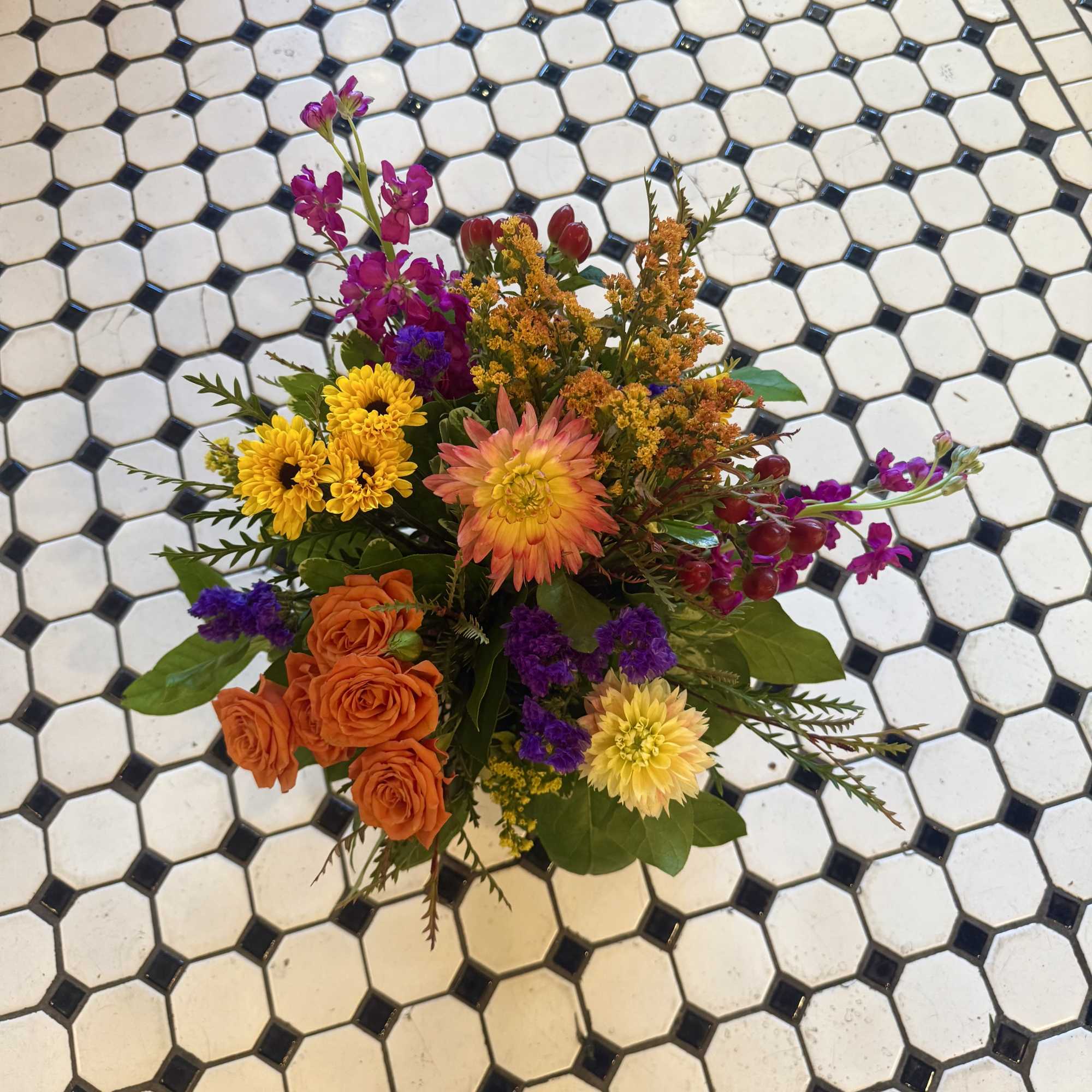 Mixed bouquet with orange roses, yellow daisies, and purple flowers on tile floor