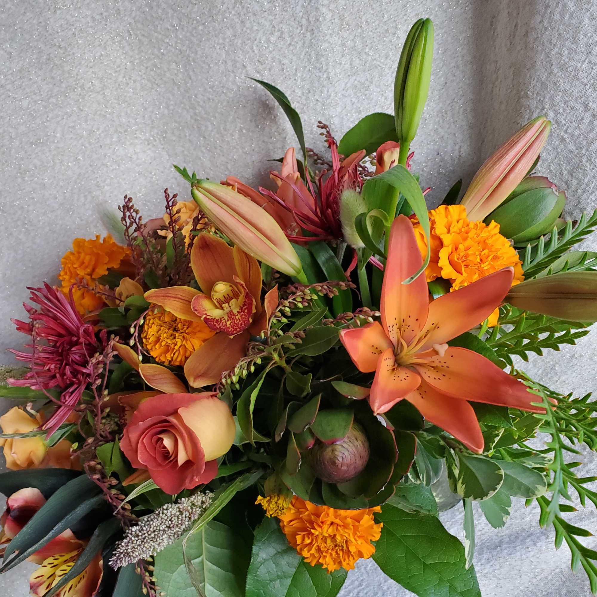 Bouquet of orange lilies, marigolds, roses, and orchids in warm autumn colors