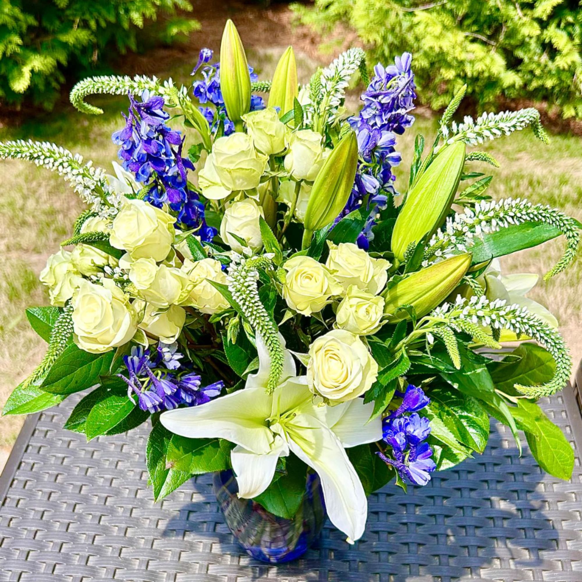 White roses and lilies with blue flowers in a glass vase