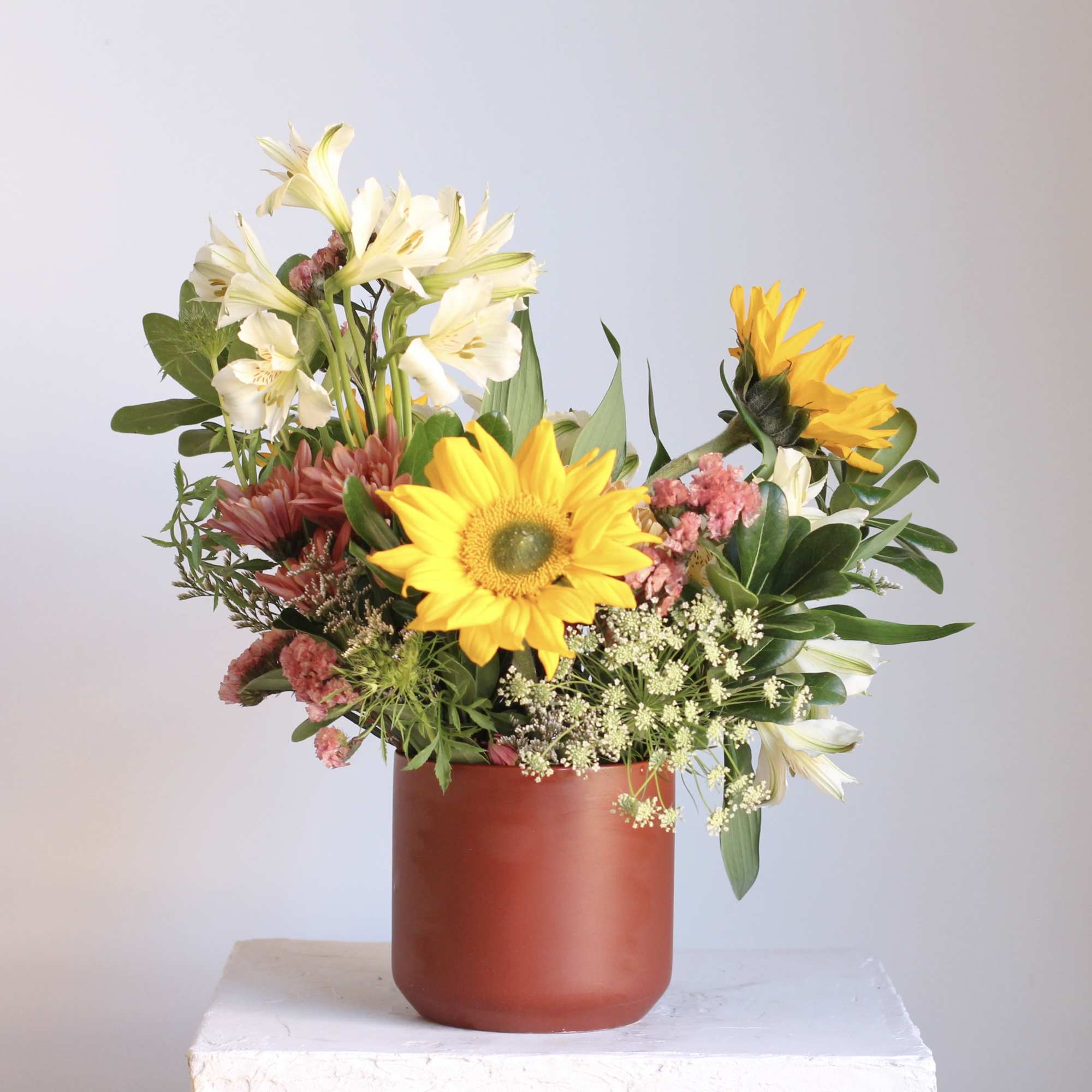 Mixed bouquet with sunflowers, white lilies, and pink flowers in a red vase