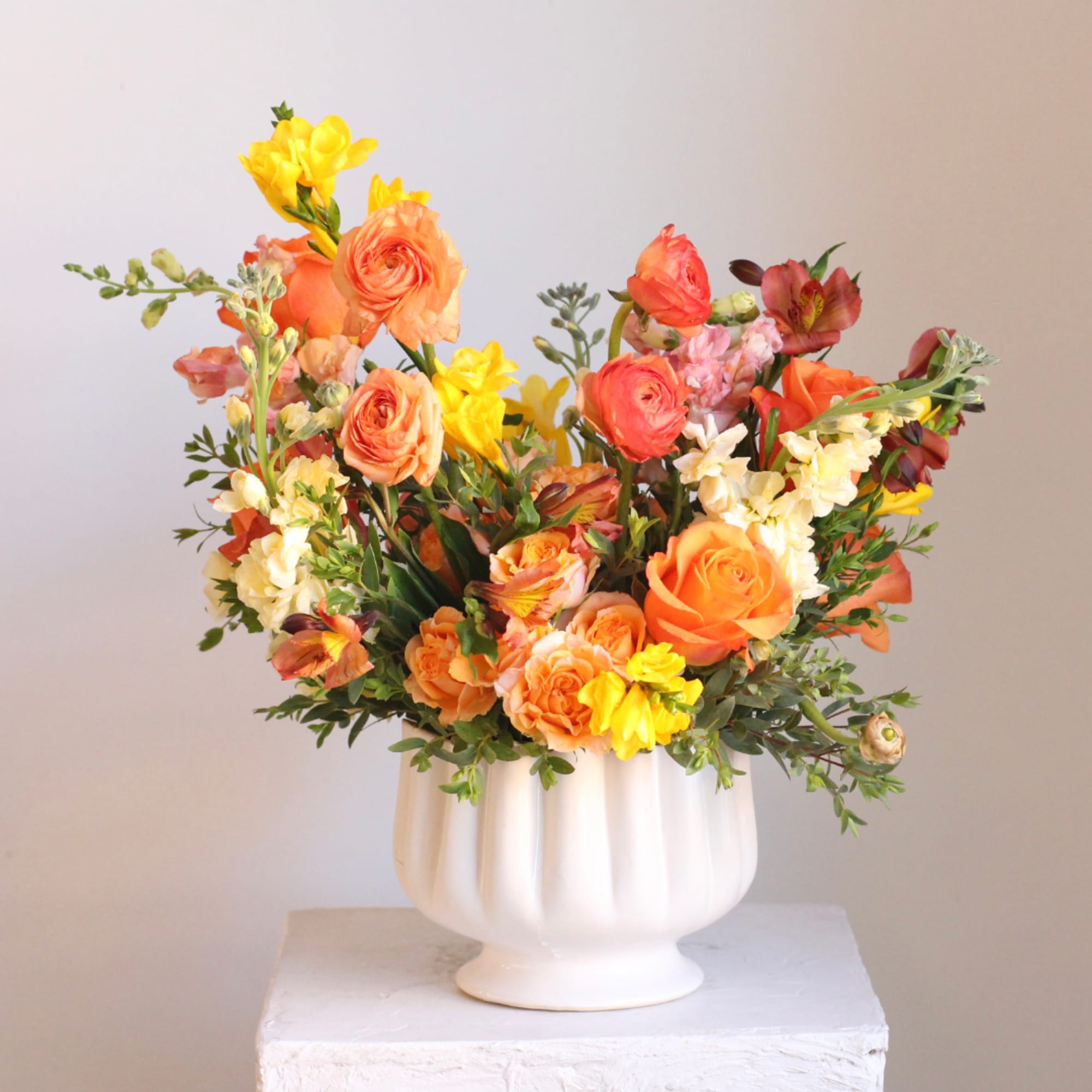 Orange and yellow mixed flower arrangement in a white vase