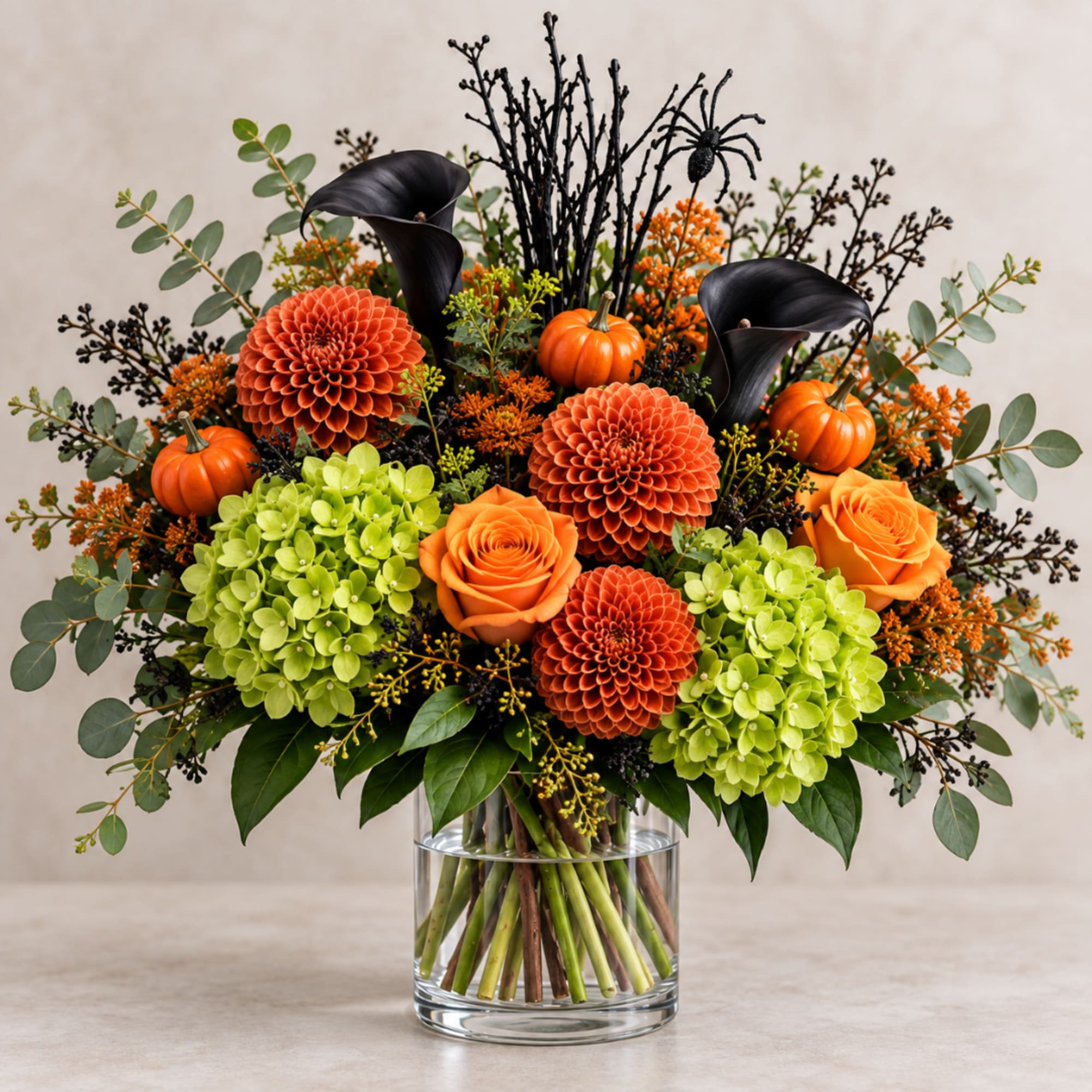 Orange and green floral arrangement in a clear glass vase with small pumpkins