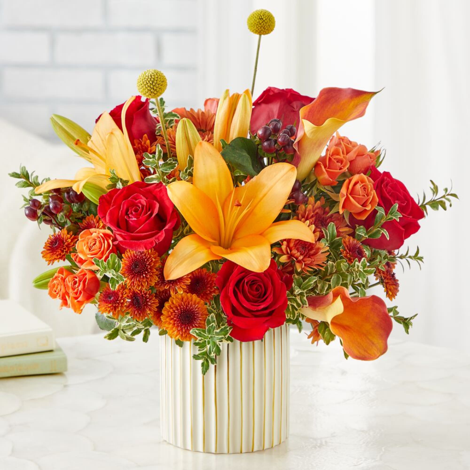 Bright mixed bouquet with red roses, yellow lilies, and orange flowers in a striped vase