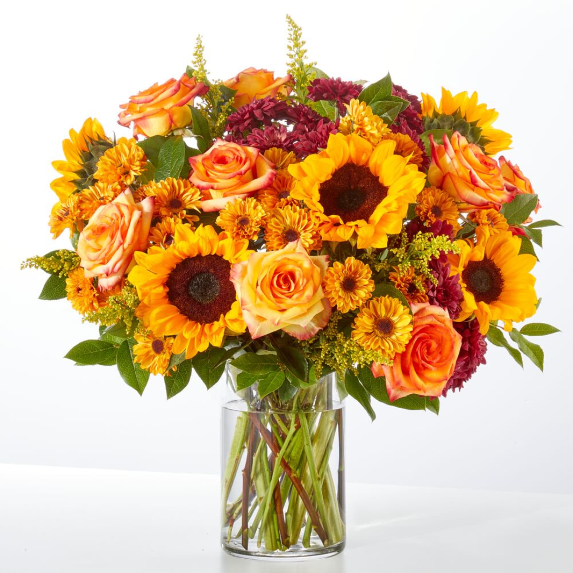 Bouquet of sunflowers, orange roses, and burgundy mums in a clear glass vase