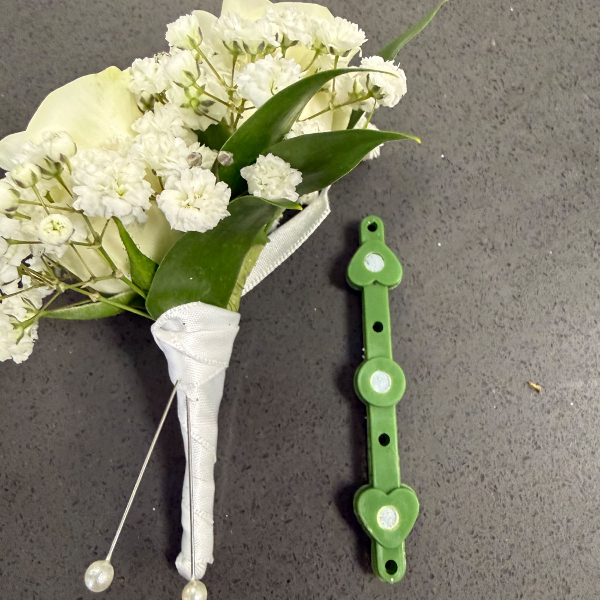 White boutonniere with small clustered blooms and green leaves beside a green pin holder