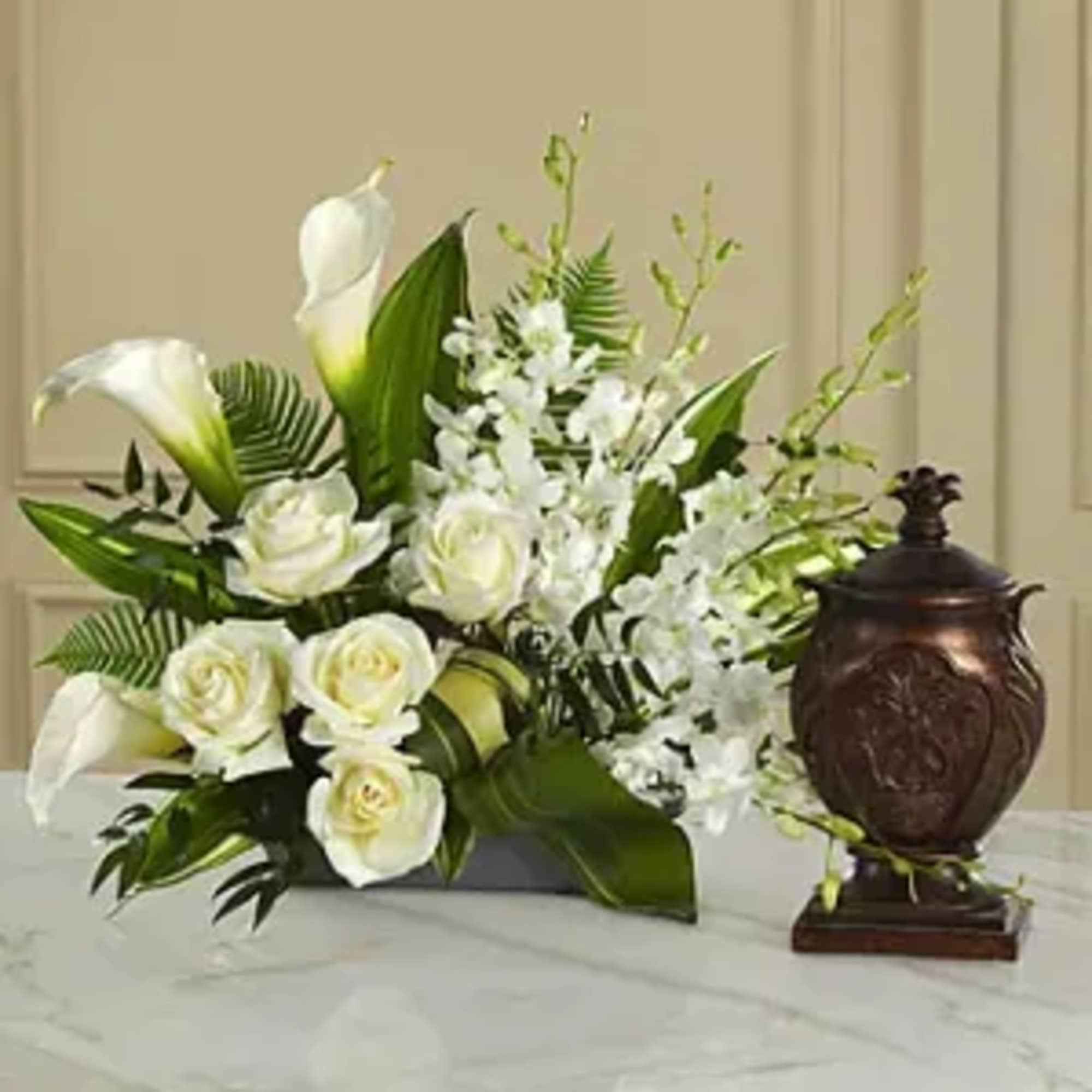 White roses and calla lilies arranged with white orchids in a dark vase
