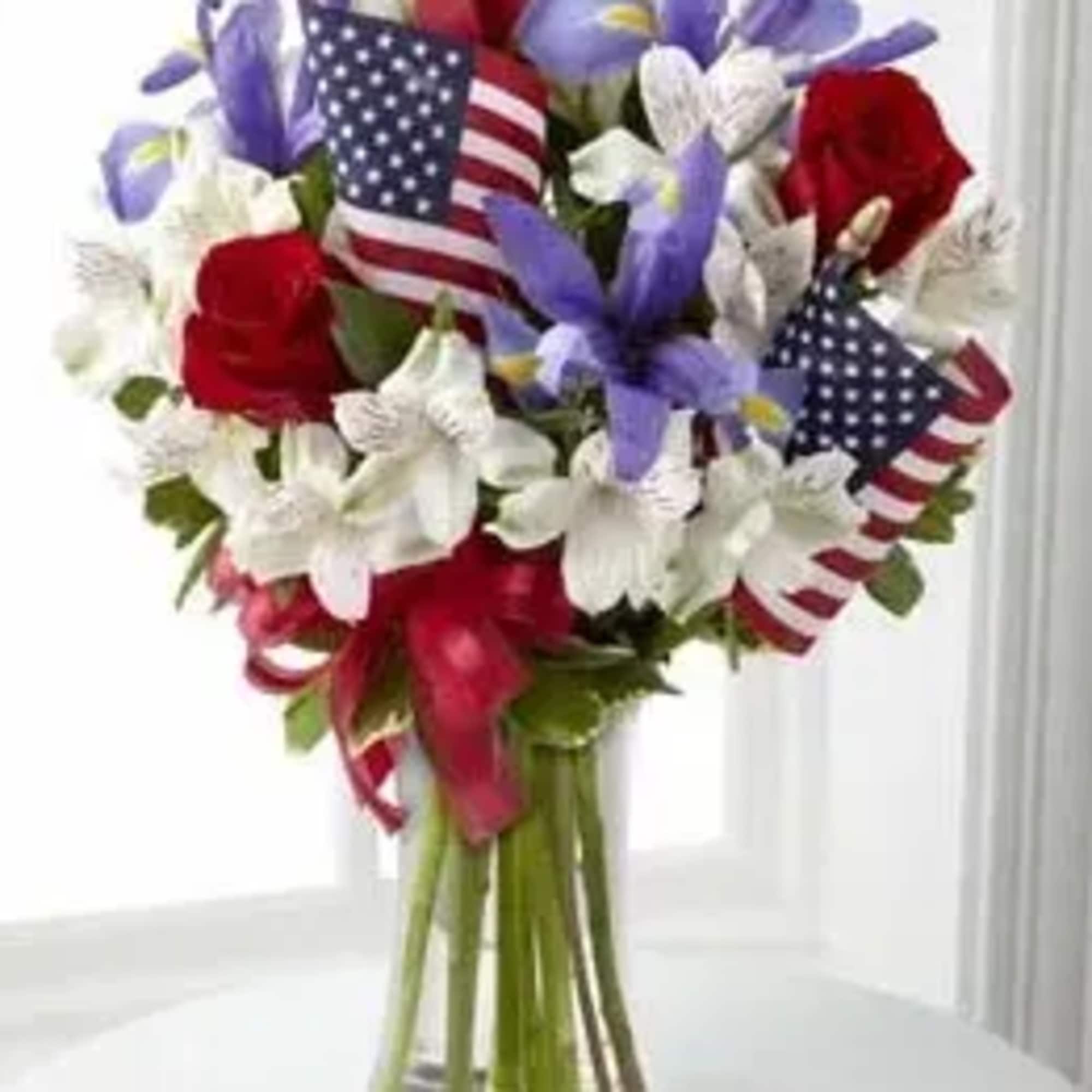 Red, white, and blue bouquet in a glass vase with small American flags