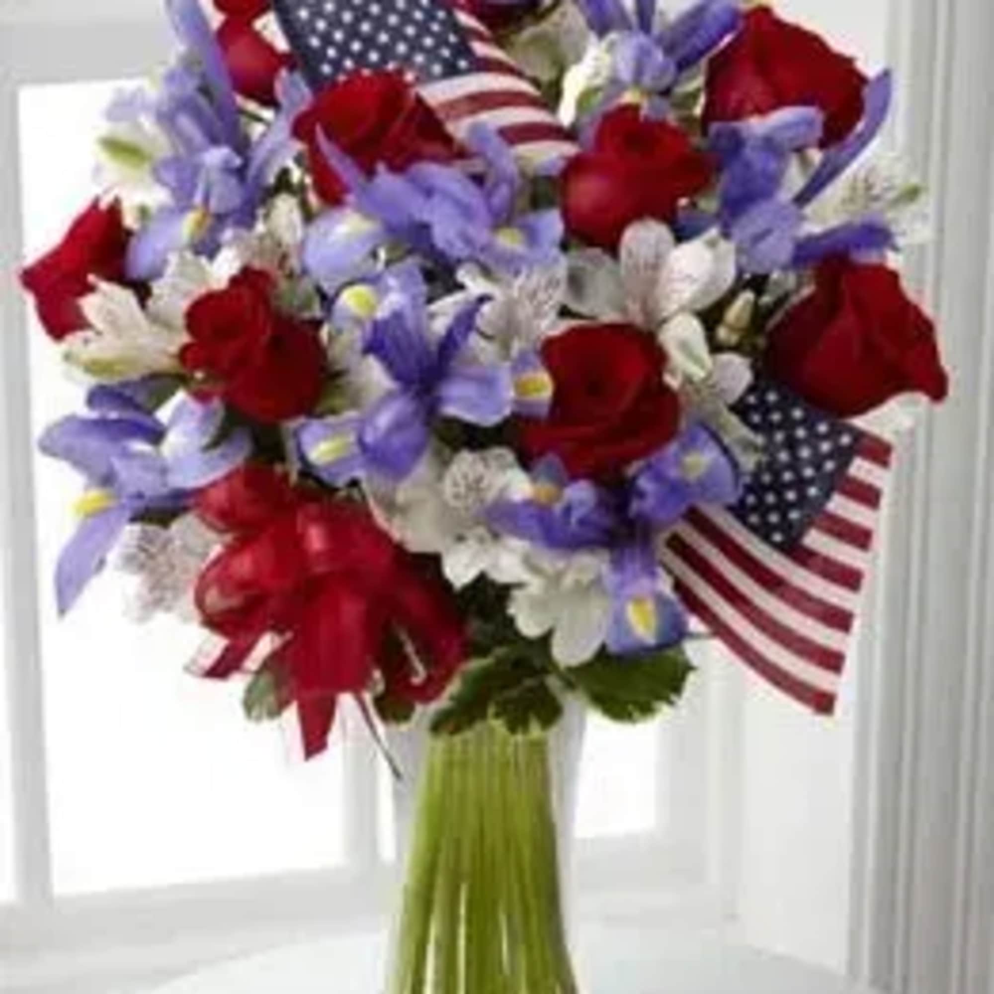 Bouquet of red, white, and purple flowers with small American flags in a glass vase