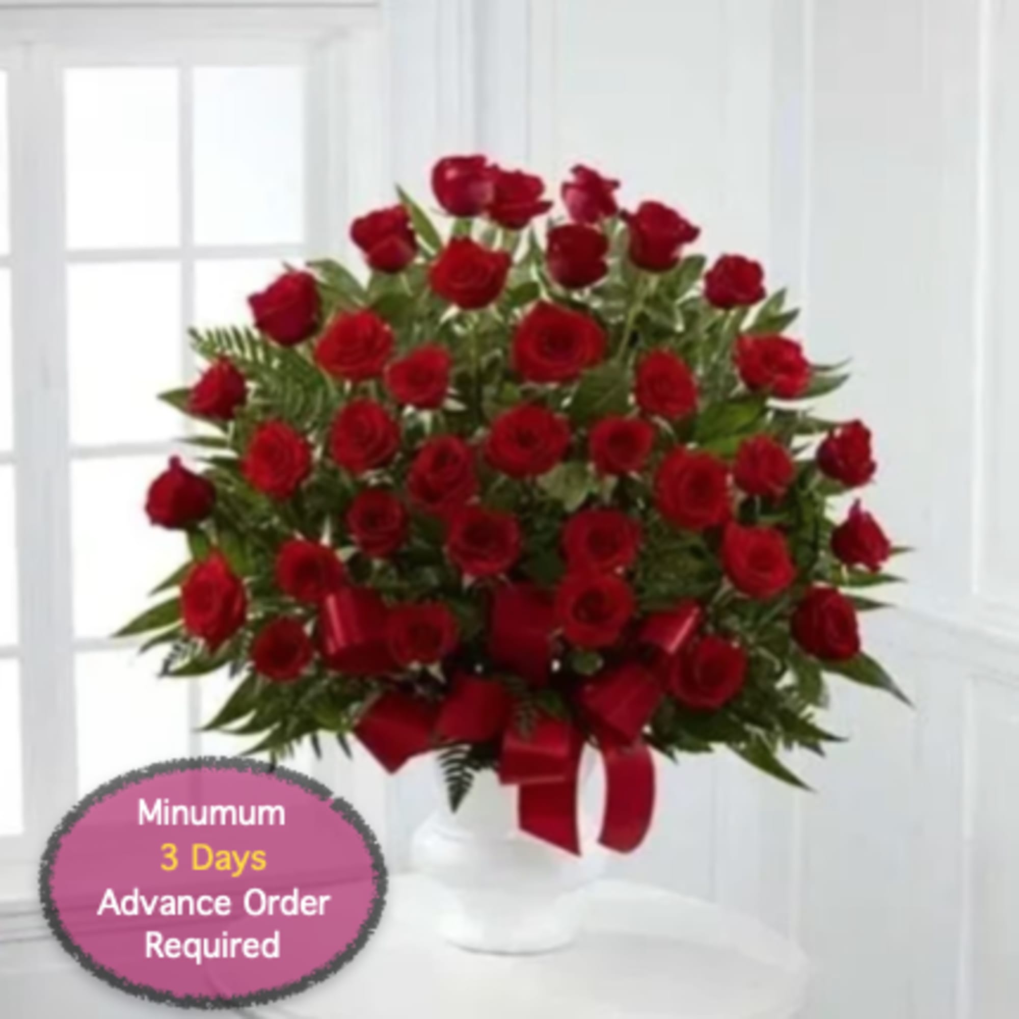 Red roses arranged in a white vase with a red ribbon