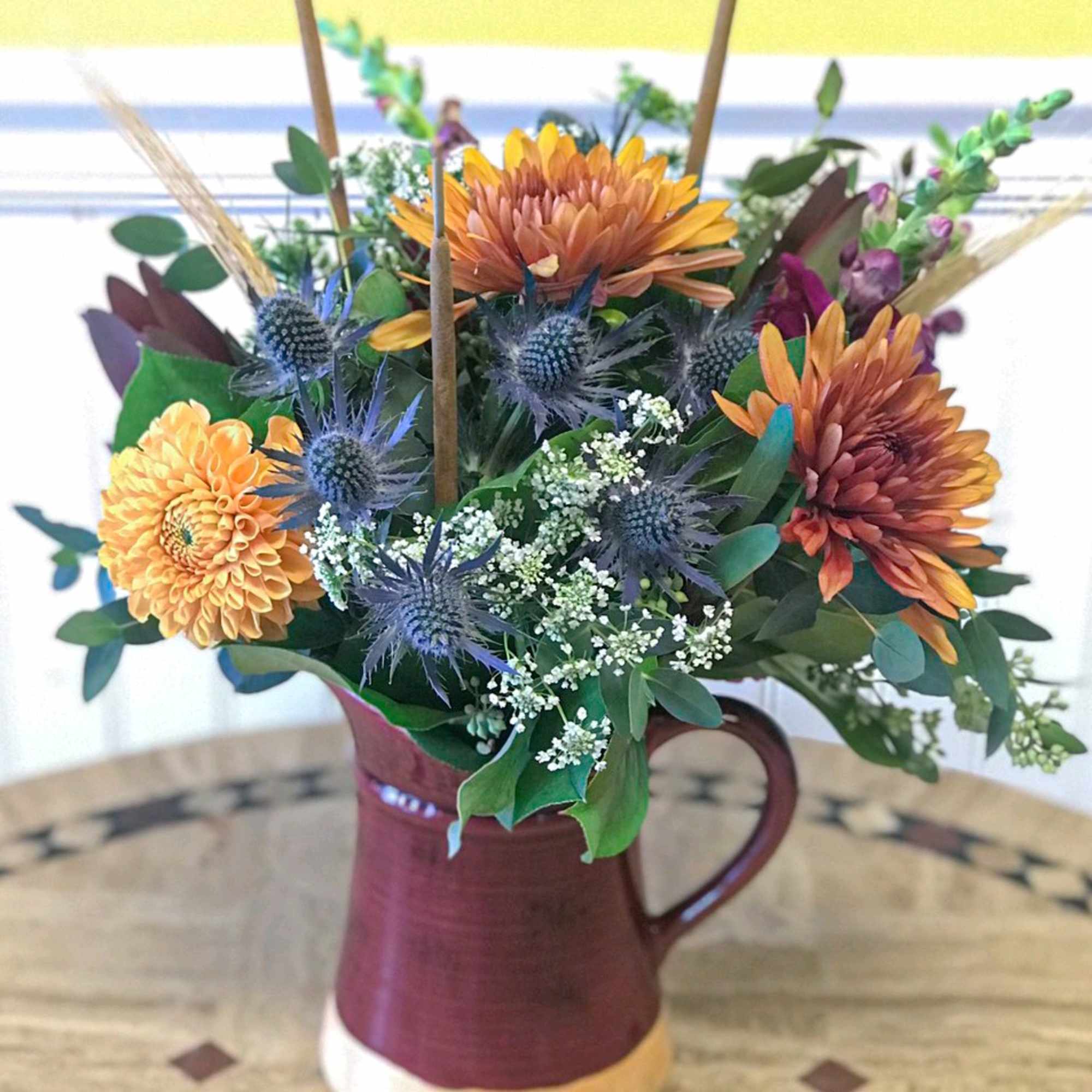 Mixed bouquet in a burgundy pitcher vase with orange and blue flowers