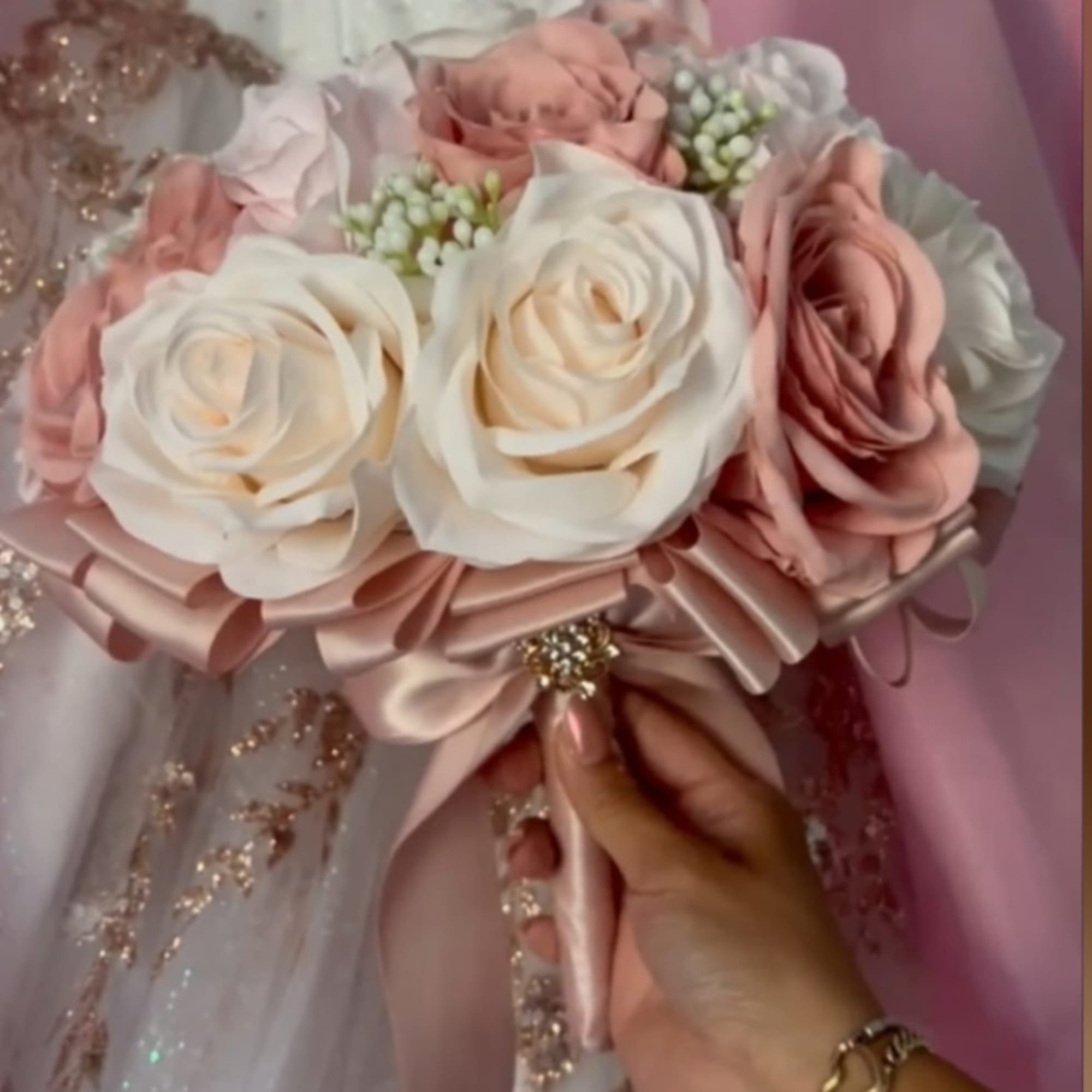 Pink and white rose bouquet with satin ribbon and a hand holding the stems