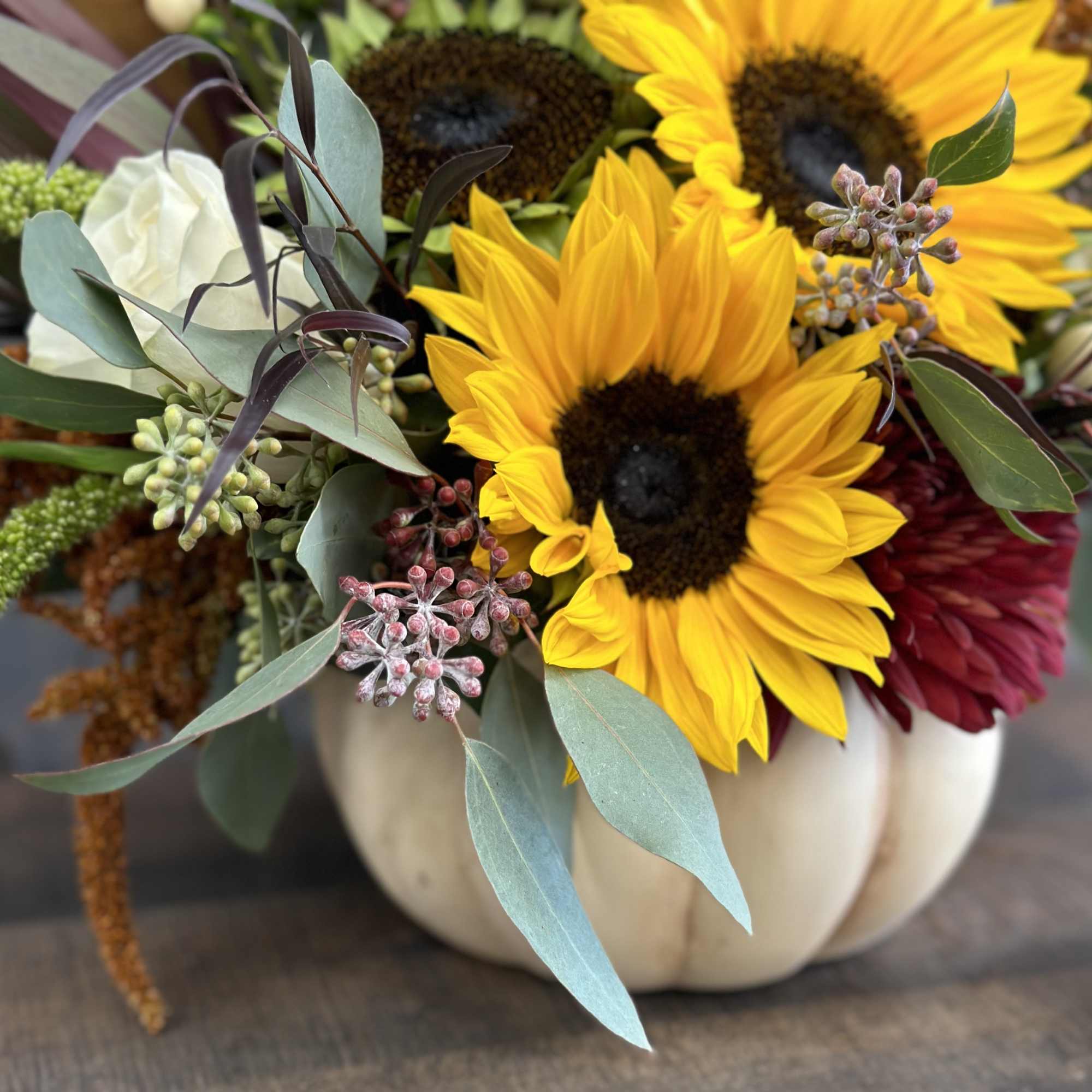 Sunflower arrangement in a white pumpkin vase with burgundy blooms