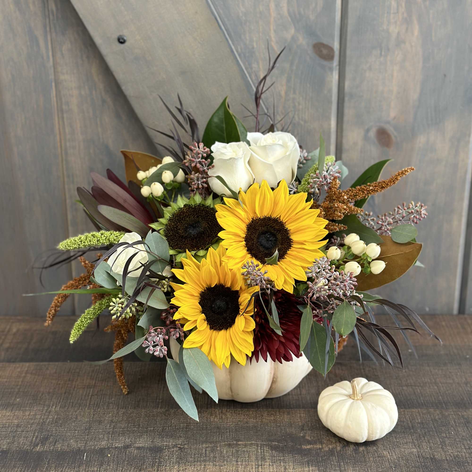 Sunflower and rose arrangement in a white pumpkin vase with a small white pumpkin beside it