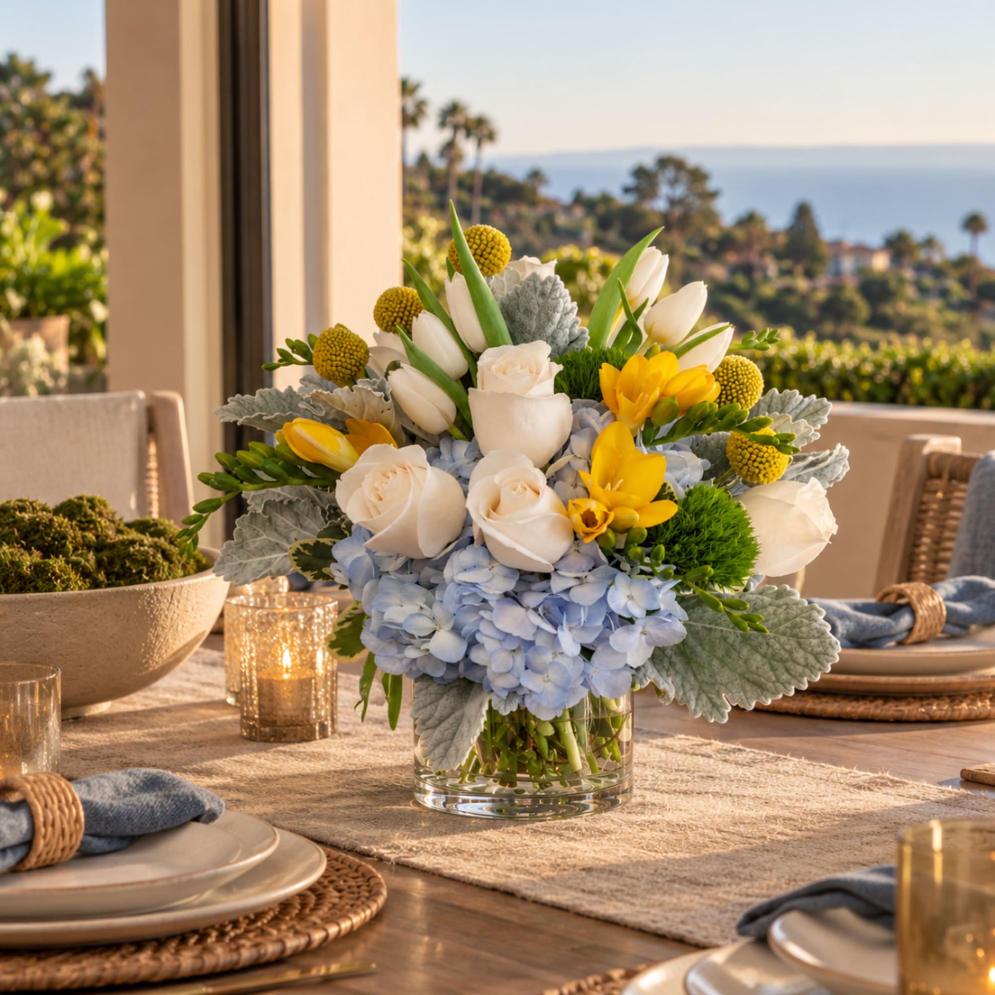 Mixed floral centerpiece in a clear glass vase with white, yellow, and blue blooms