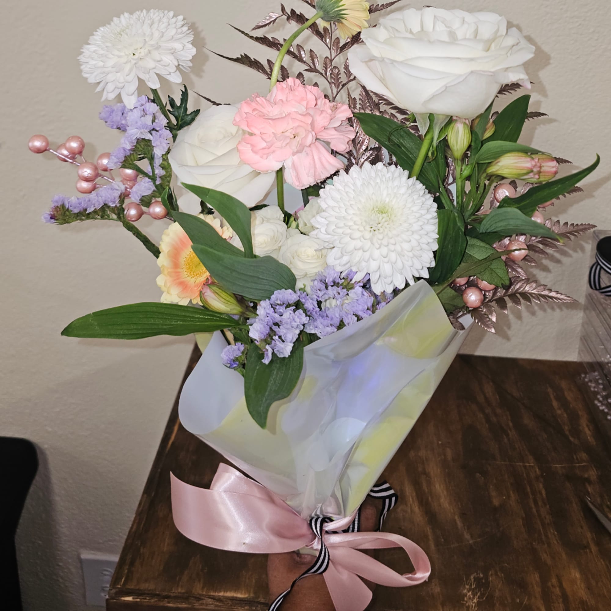 Bouquet of white roses, white mums, pink carnations, and purple filler flowers in wrap
