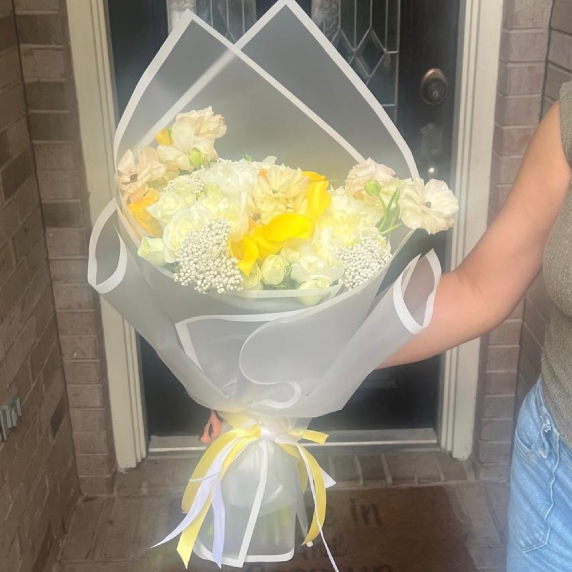 Bouquet of white and yellow flowers wrapped in translucent paper with ribbon