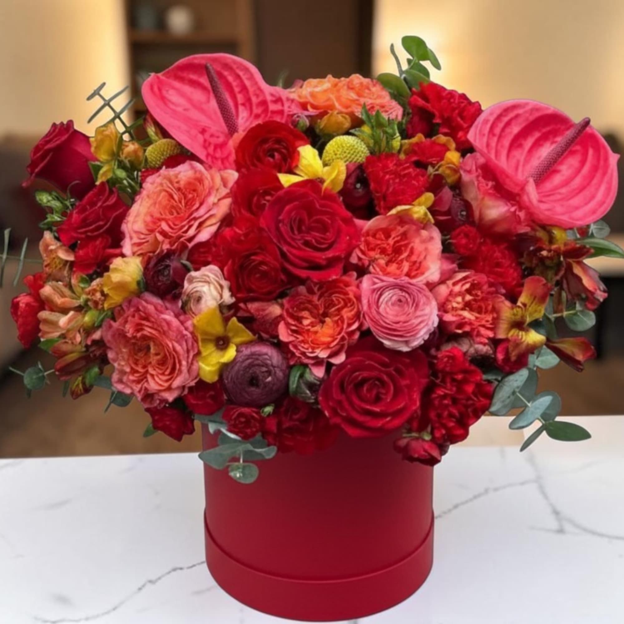 Red and pink floral arrangement in a round red box
