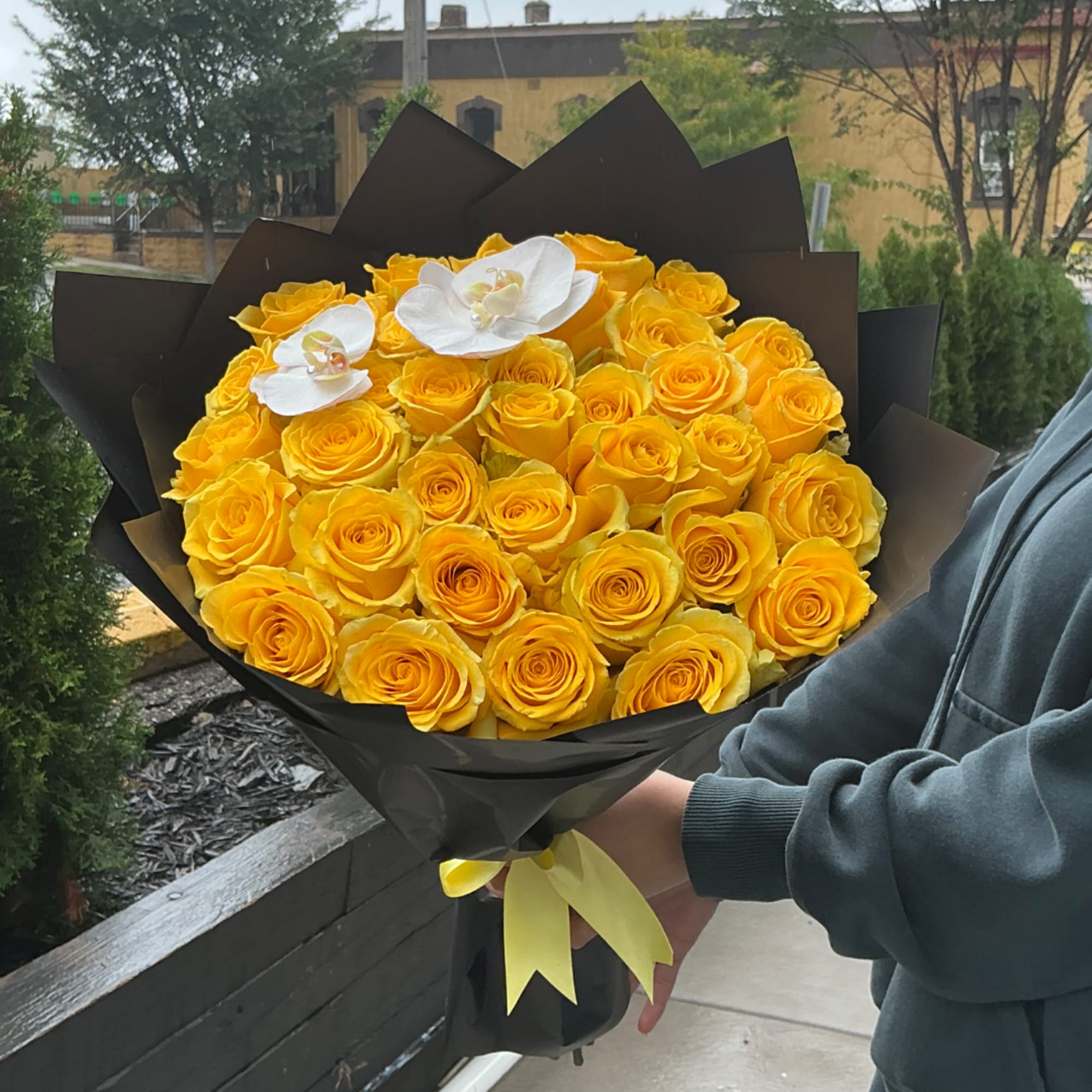 Bouquet of yellow roses with two white orchids in black wrap
