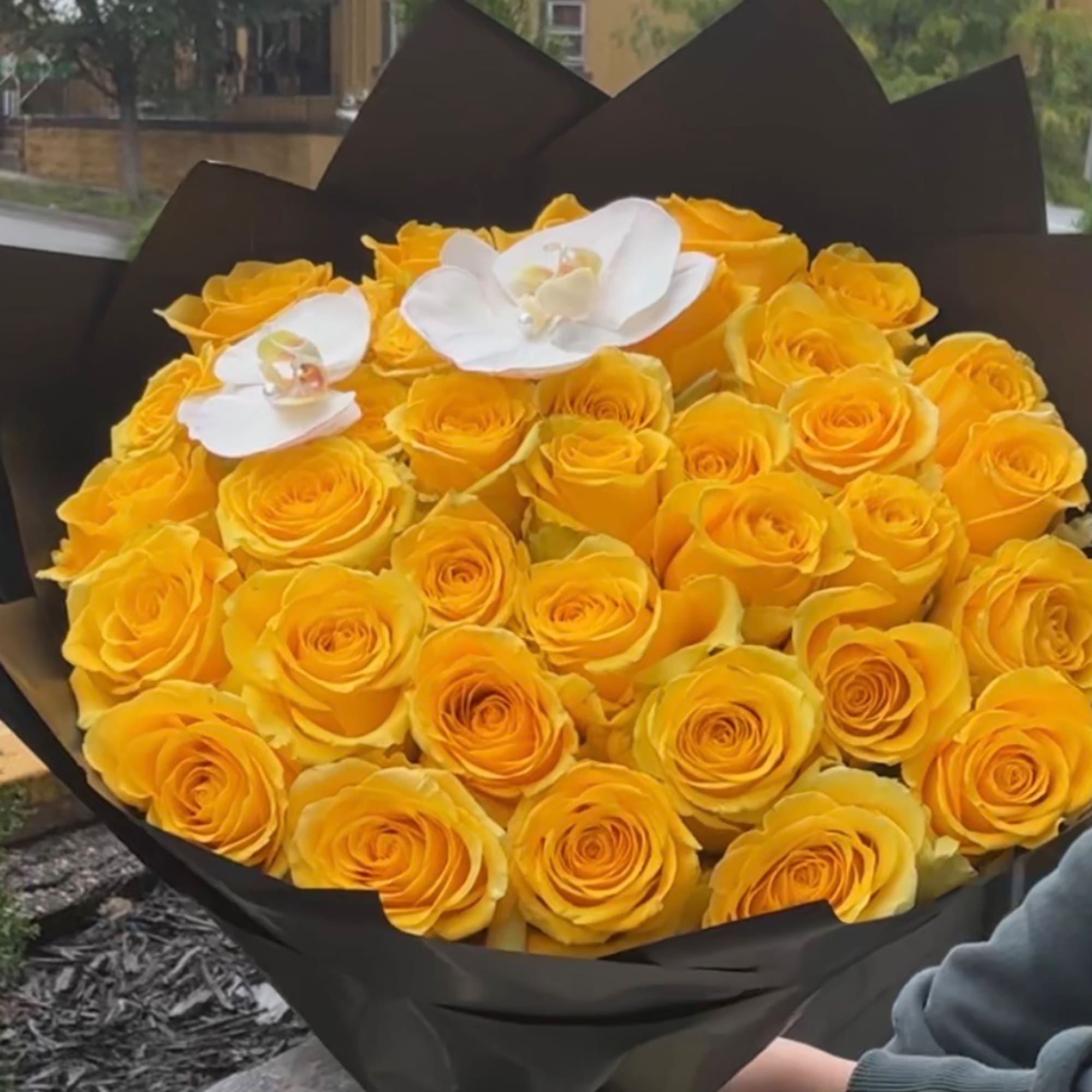 Bouquet of yellow roses with two white orchids wrapped in black paper