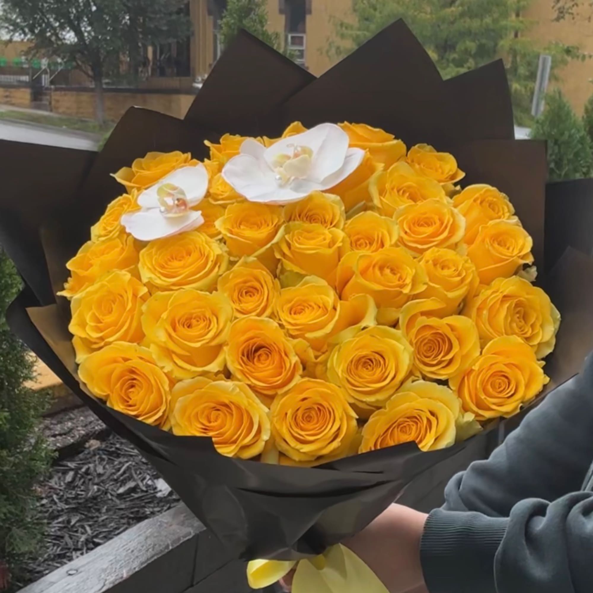 Bouquet of yellow roses with two white orchids wrapped in black paper