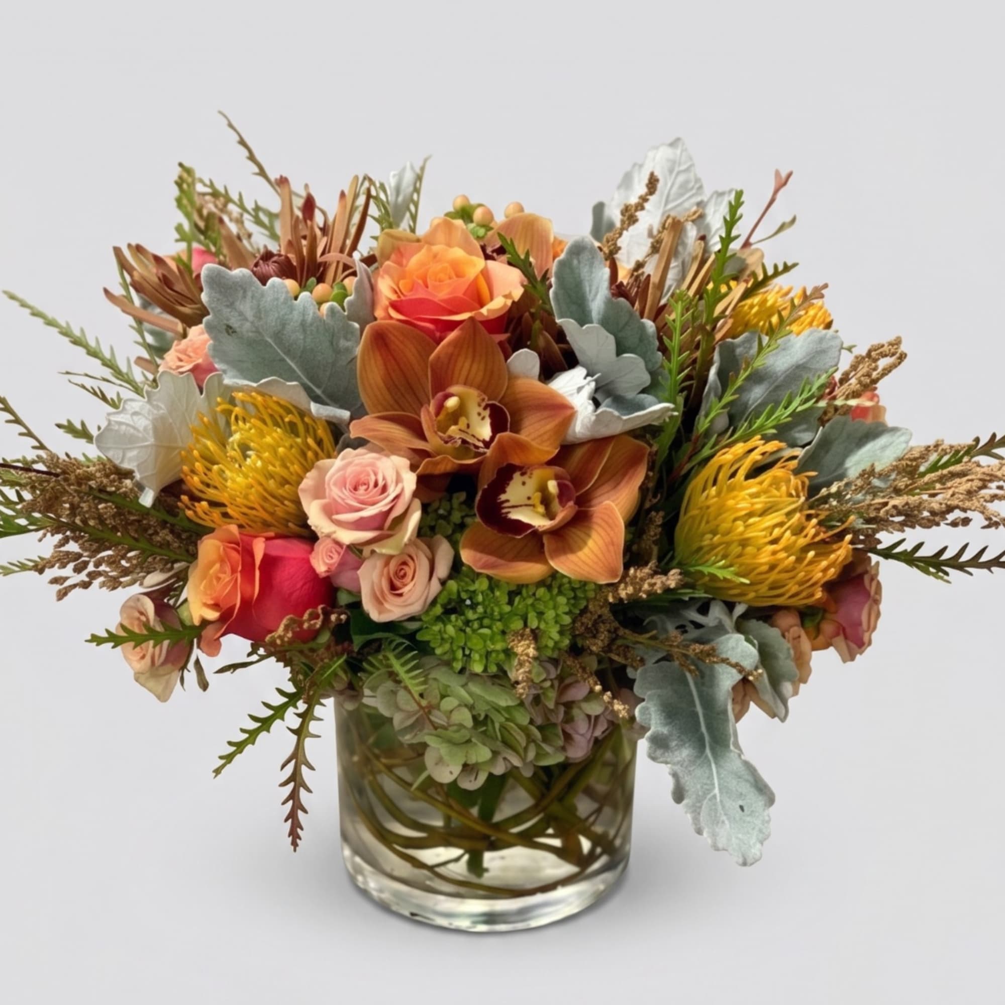 Mixed bouquet of orange, pink, and yellow flowers in a clear glass vase
