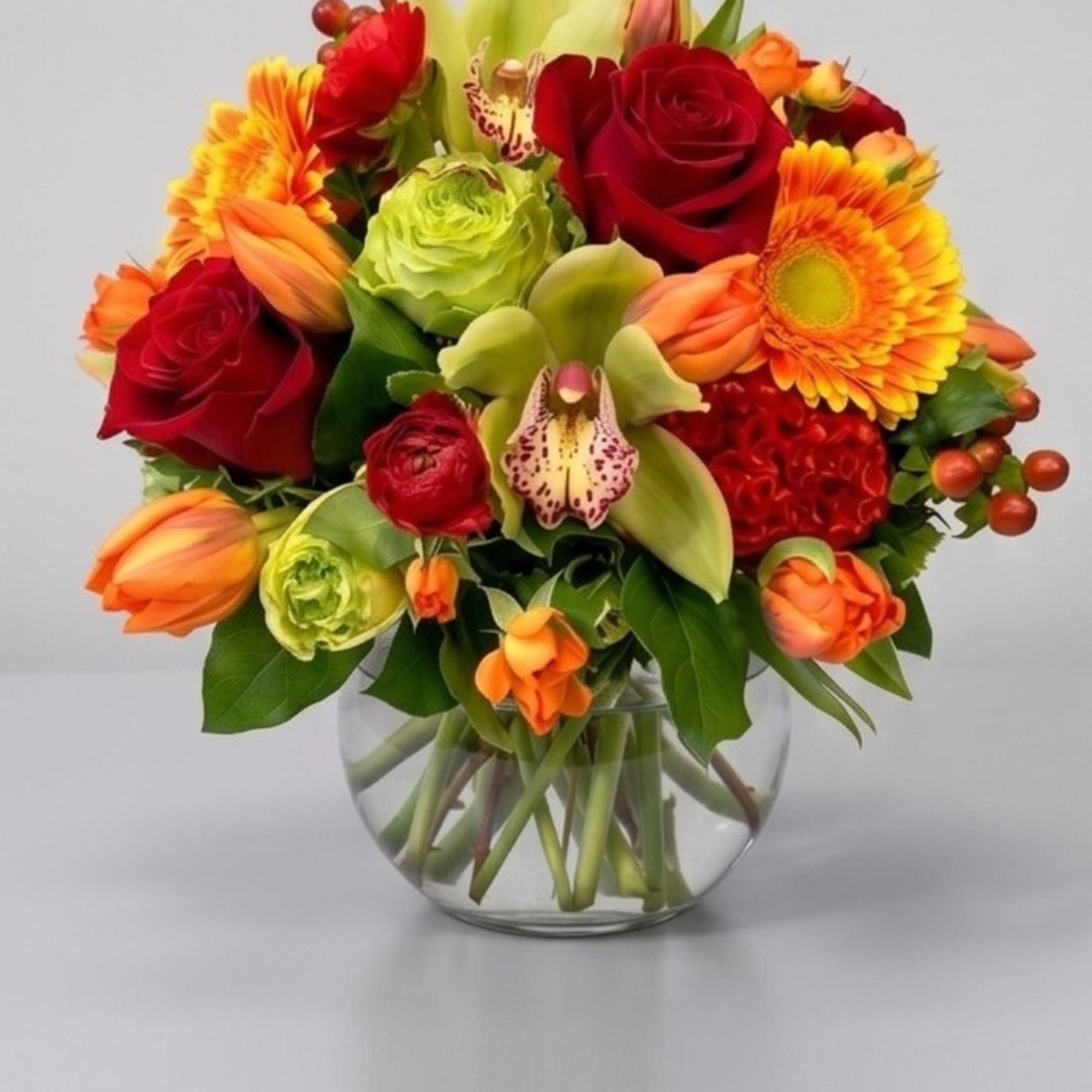 Mixed bouquet of red roses, orange tulips, and gerbera daisies in a glass vase