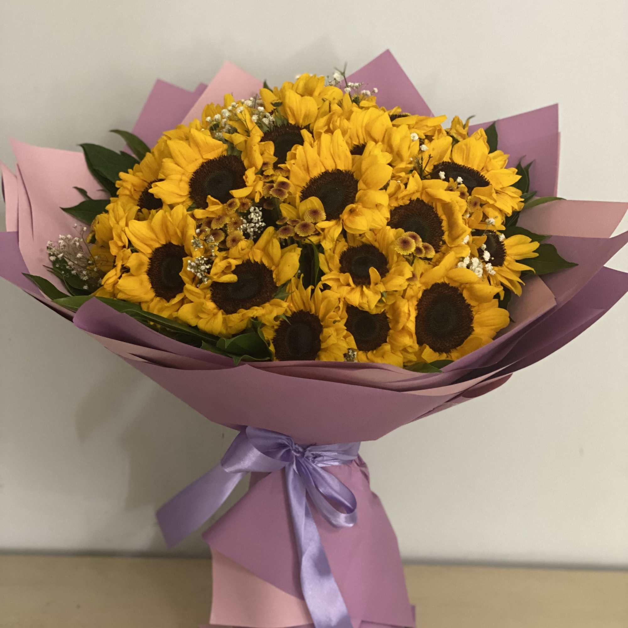 Bouquet of yellow sunflowers wrapped in pink paper with a lavender ribbon