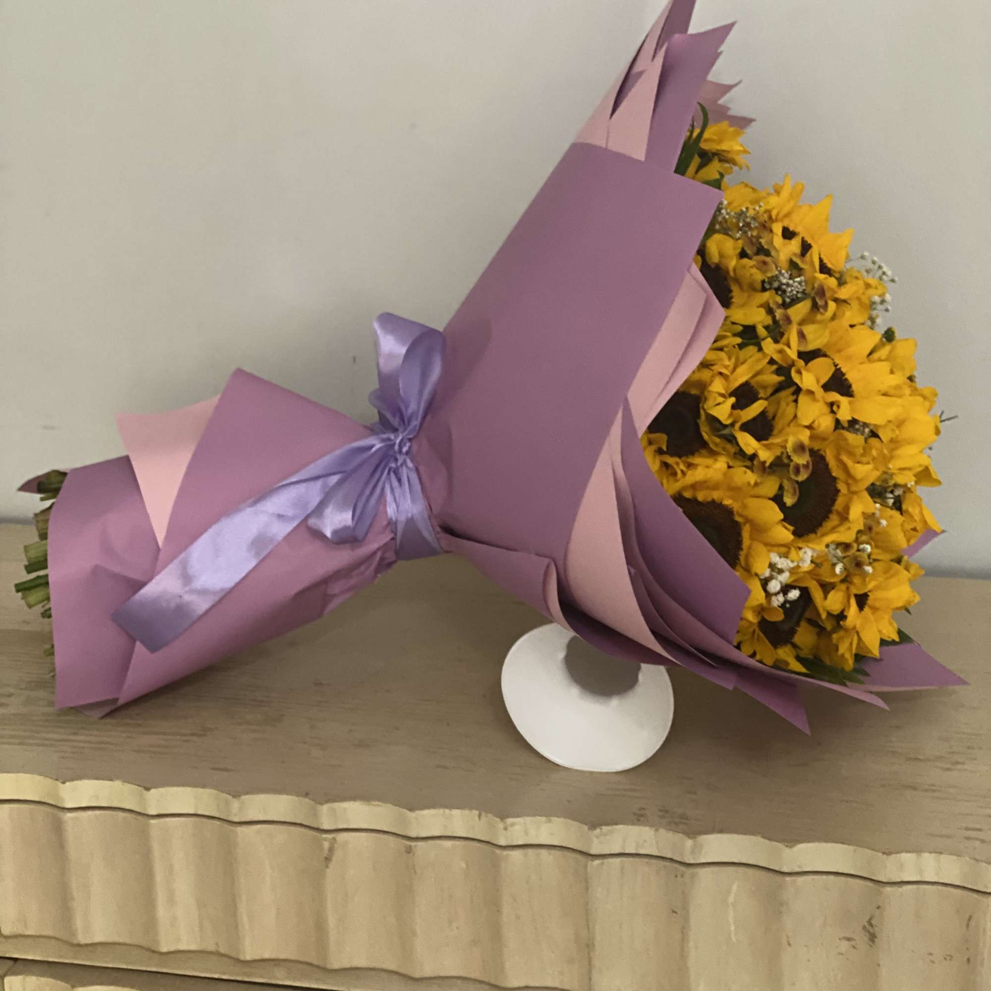 Yellow flower bouquet wrapped in purple paper with a lavender ribbon