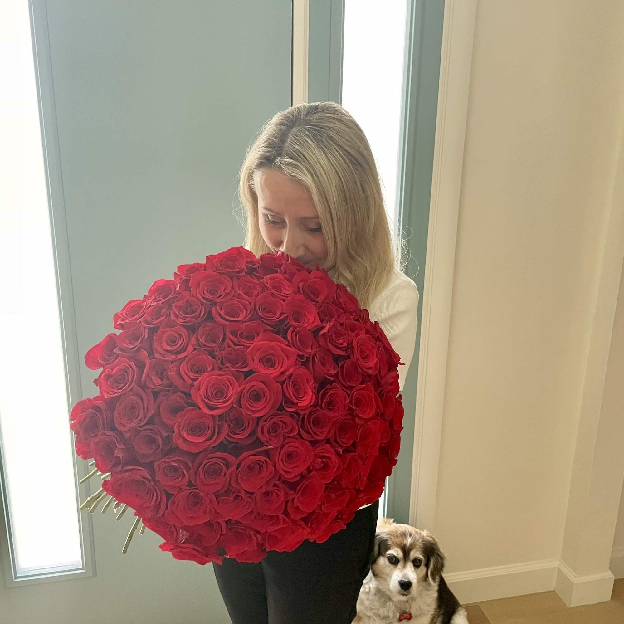 Woman holding a large bouquet of red roses with a dog beside her