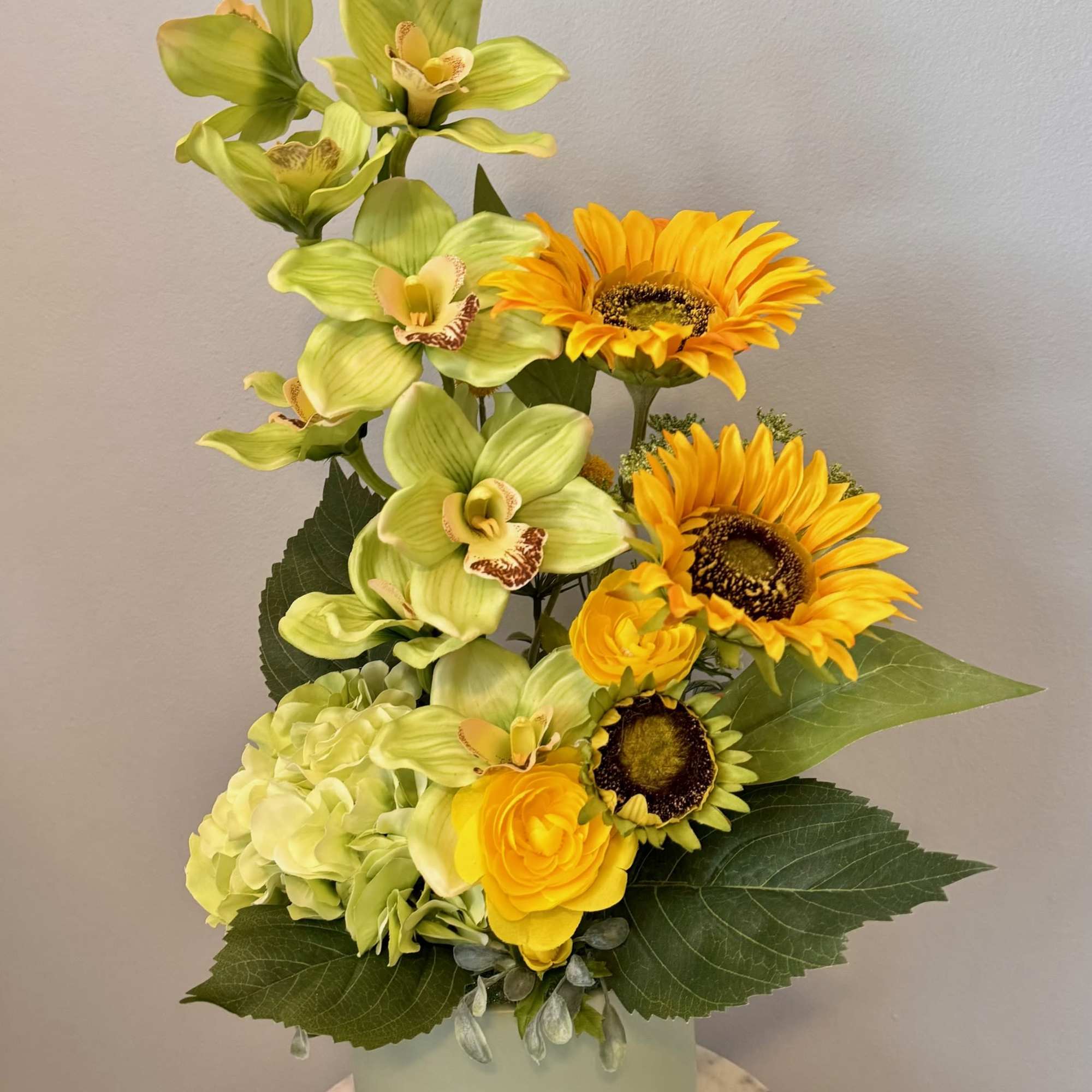 Yellow-green orchids and sunflowers in a pale vase