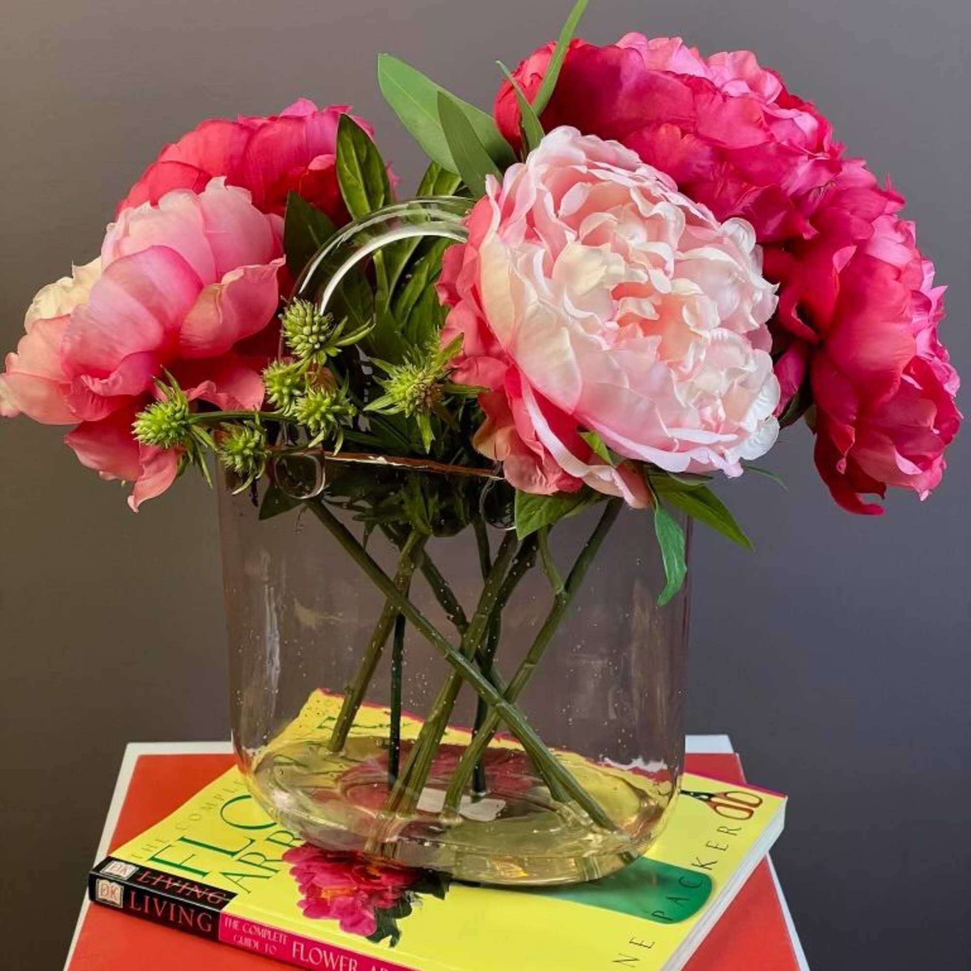 Pink peonies arranged in a clear glass vase on stacked books