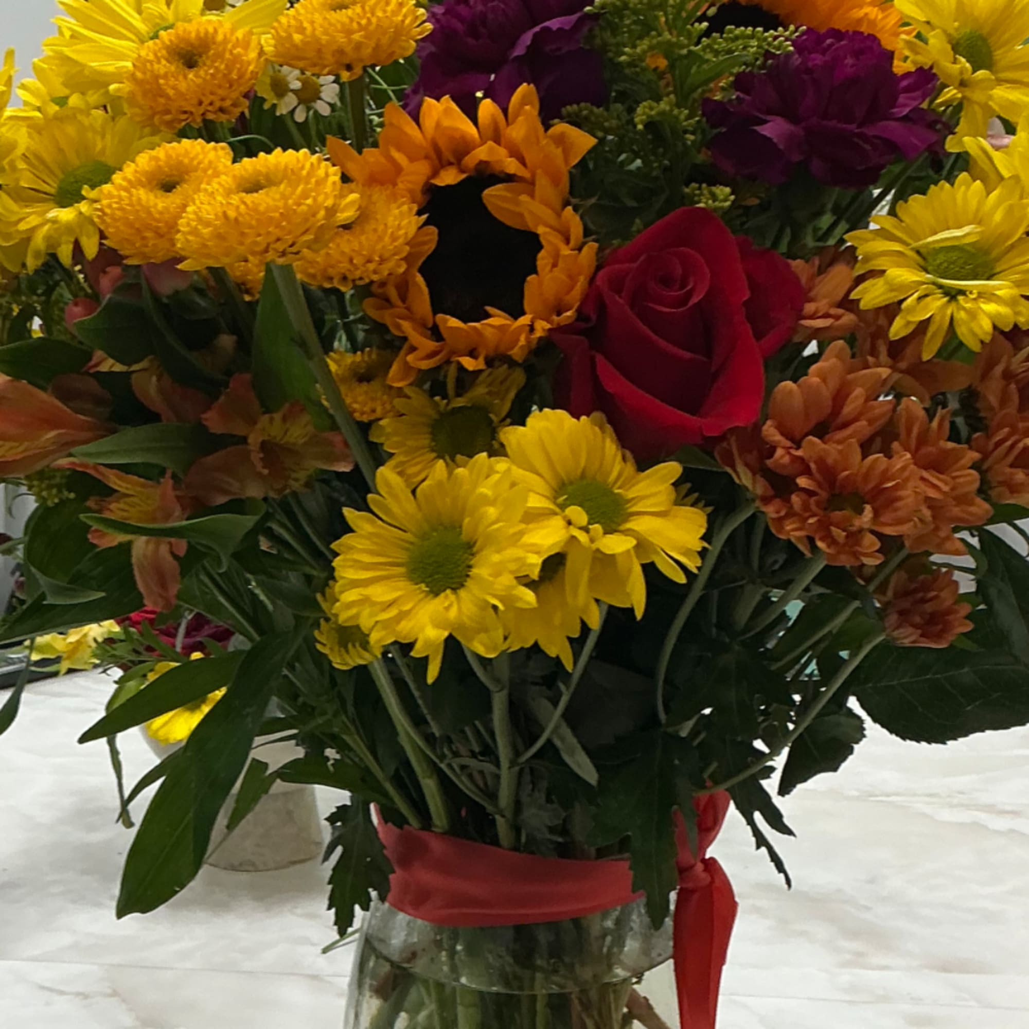 Mixed bouquet of yellow daisies, chrysanthemums, and red roses in a glass vase