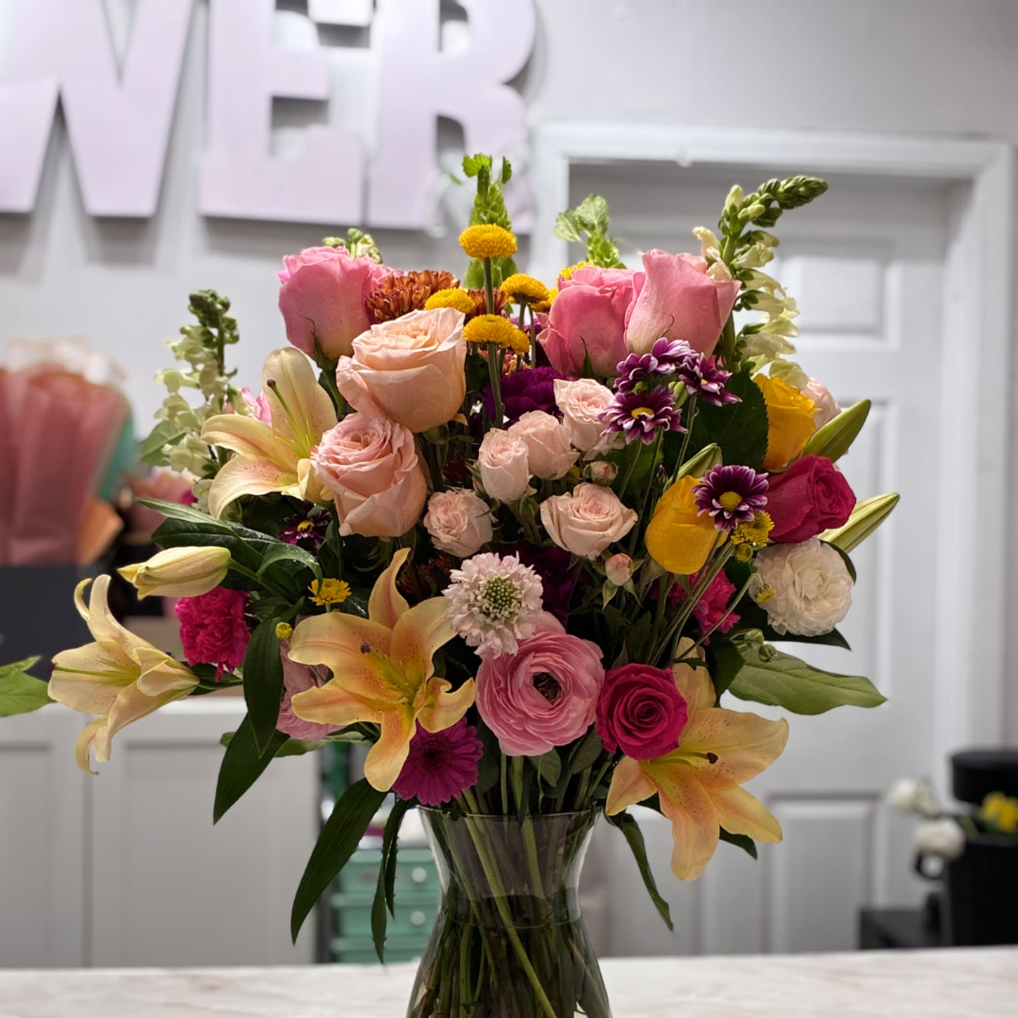 Mixed bouquet of pink, peach, yellow, and purple flowers in a glass vase