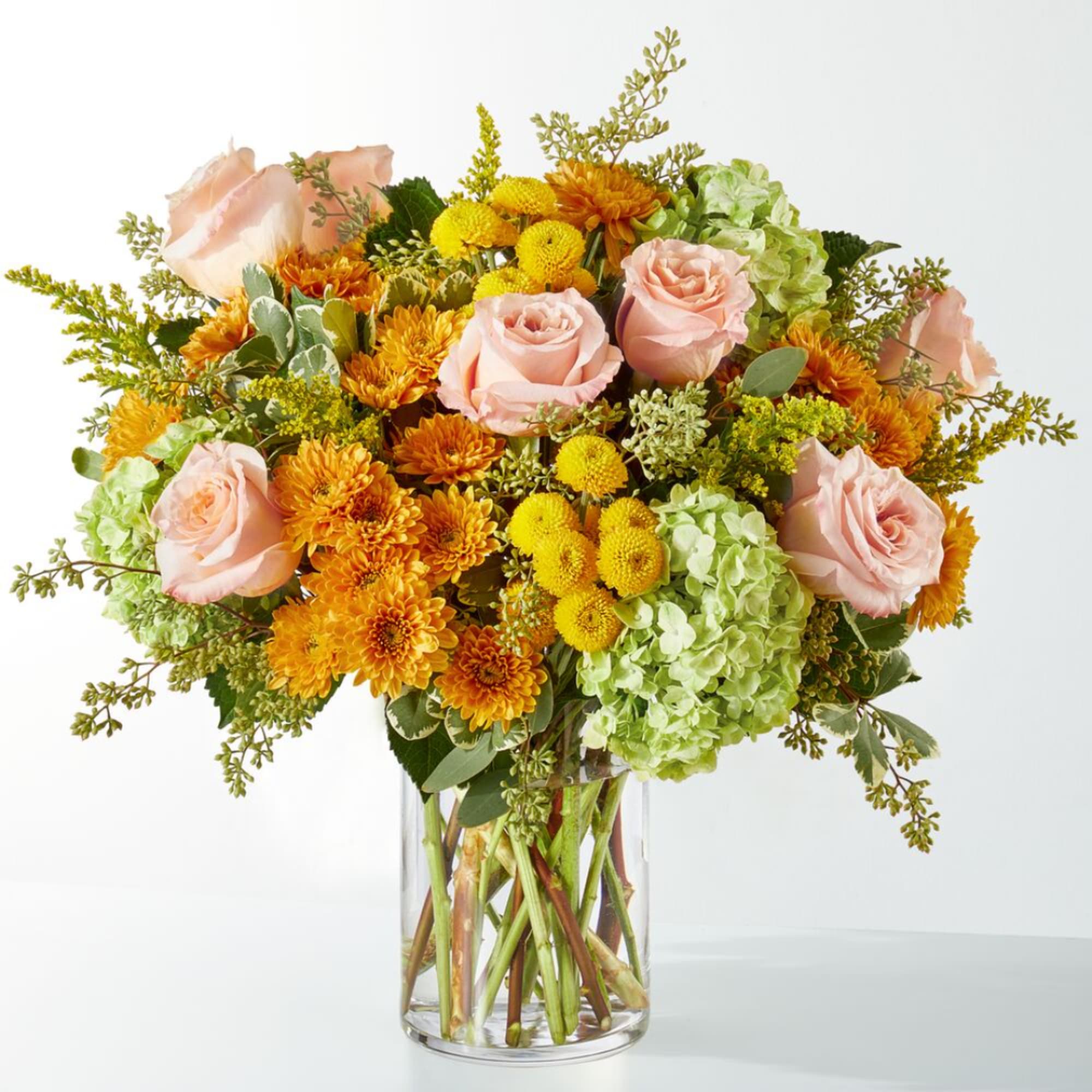 Bouquet of pink roses, orange mums, and green hydrangeas in a clear glass vase