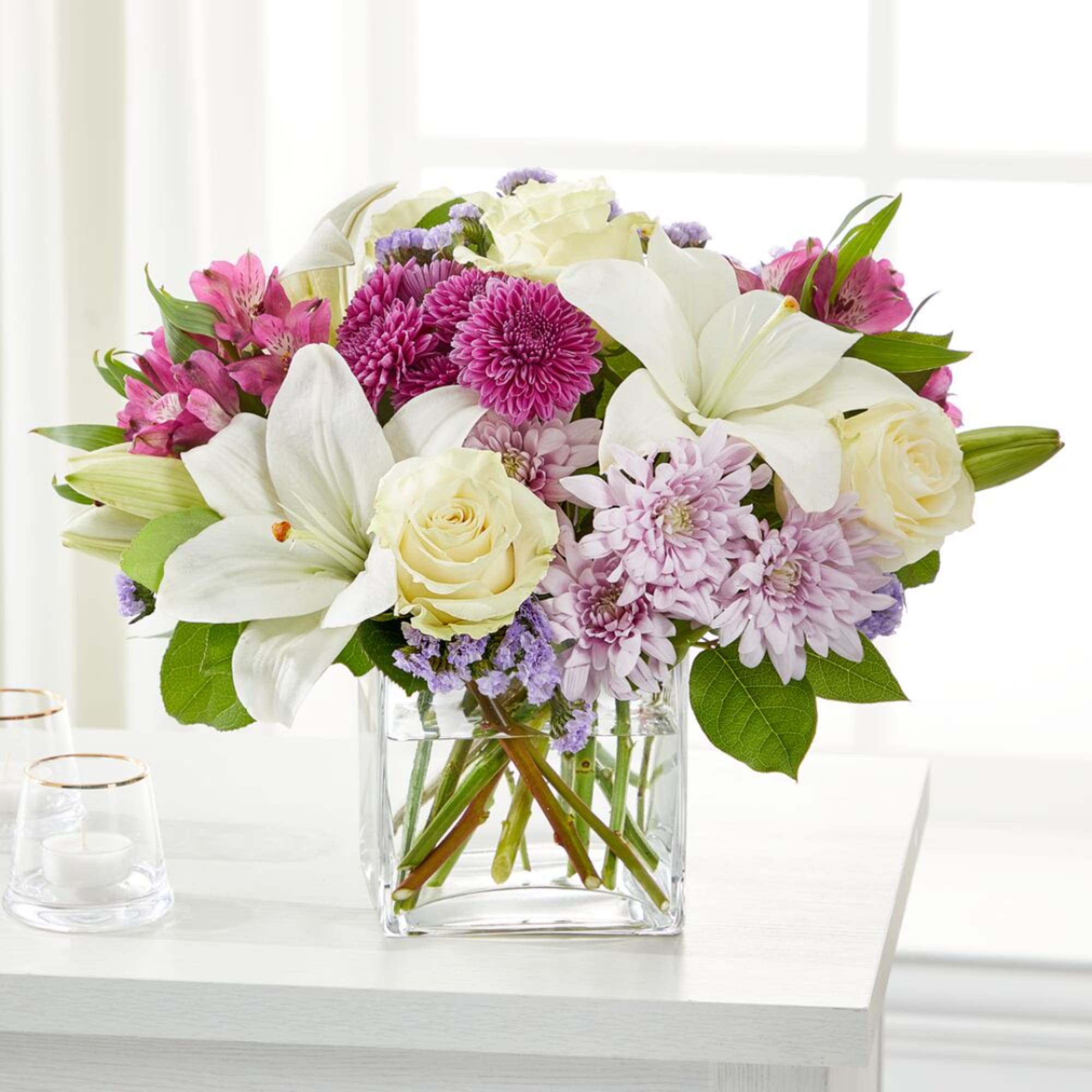 Bouquet of white lilies, cream roses, and pink chrysanthemums in a glass vase