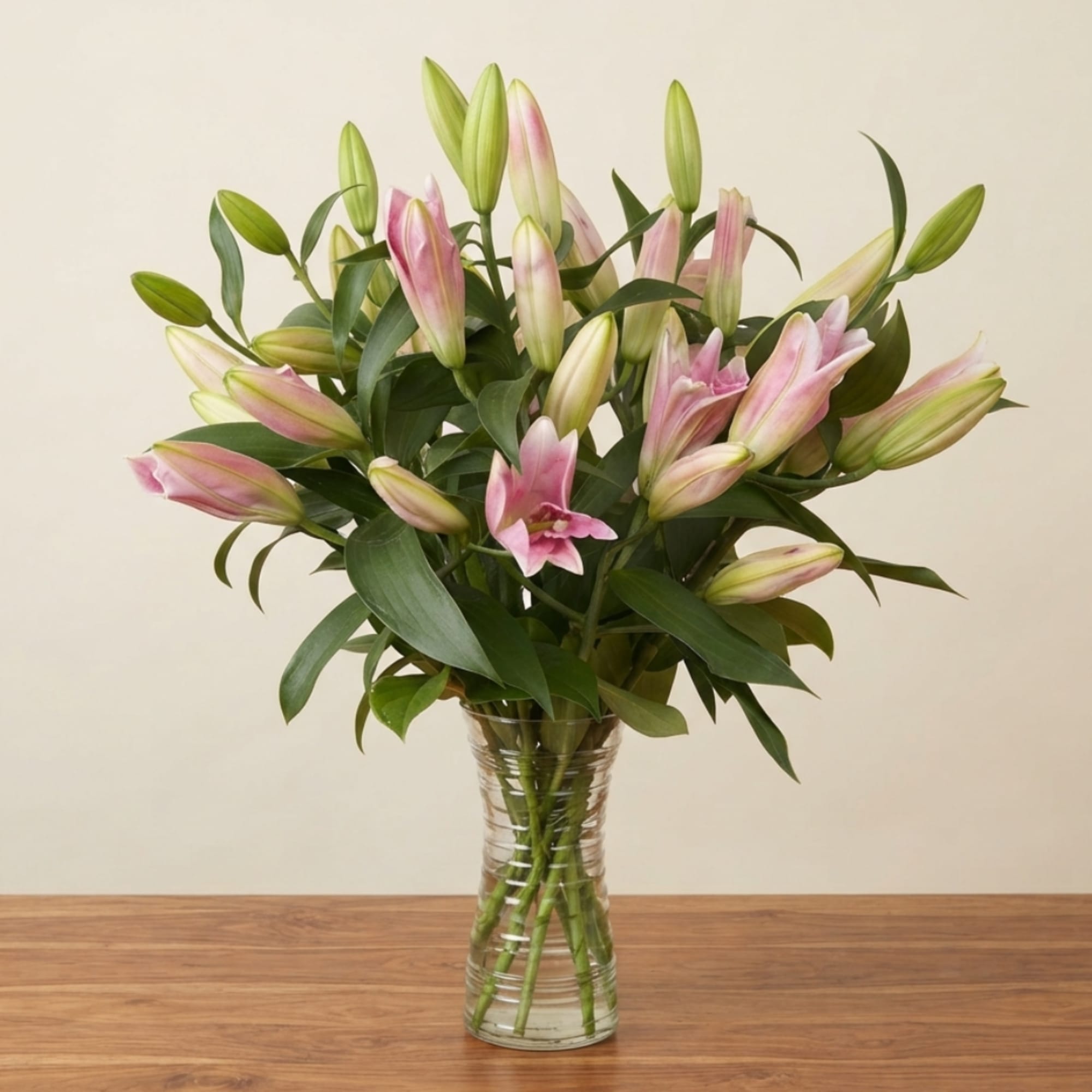 Pink lilies in a clear glass vase on a wooden table