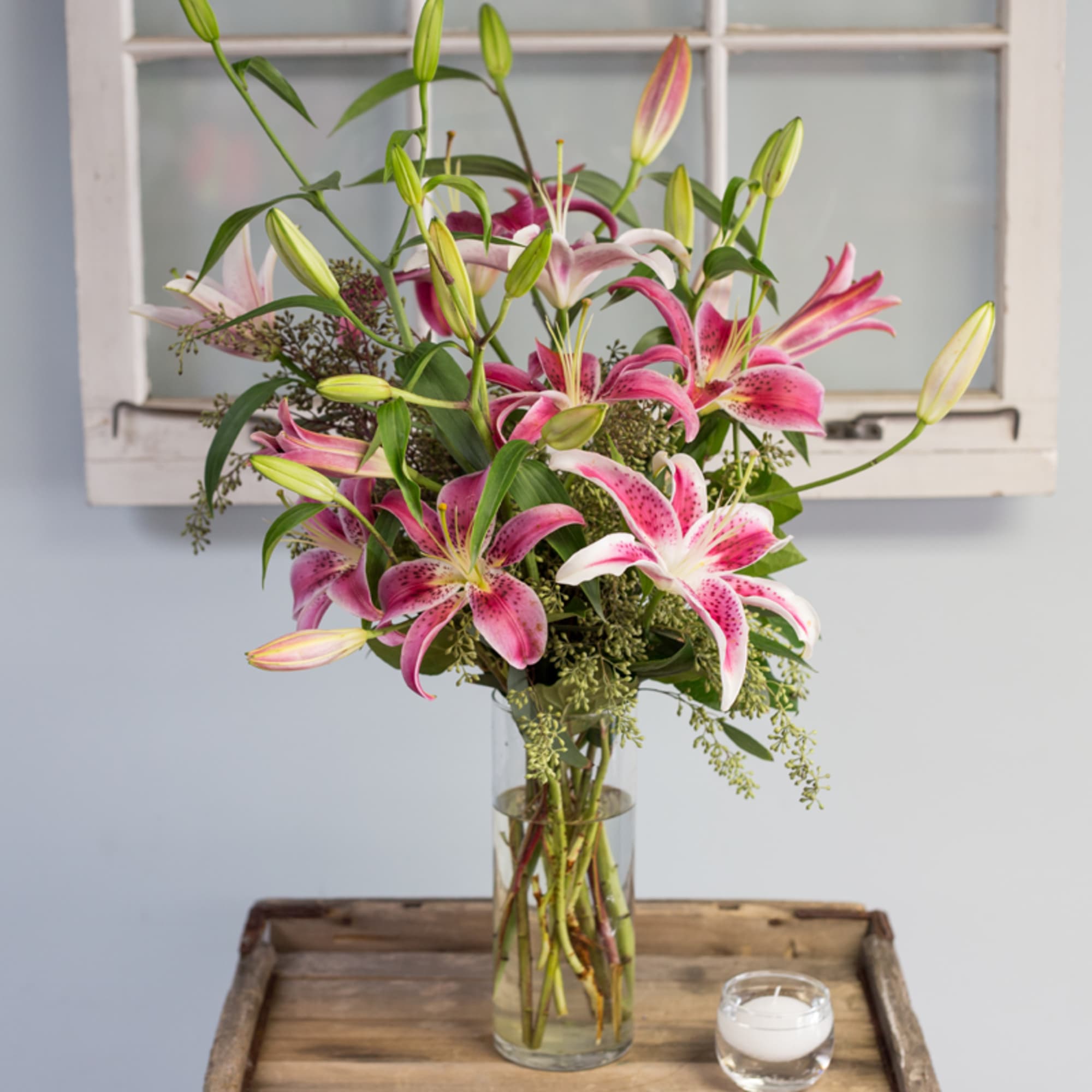 Pink and white lilies in a clear glass vase on a wooden tray
