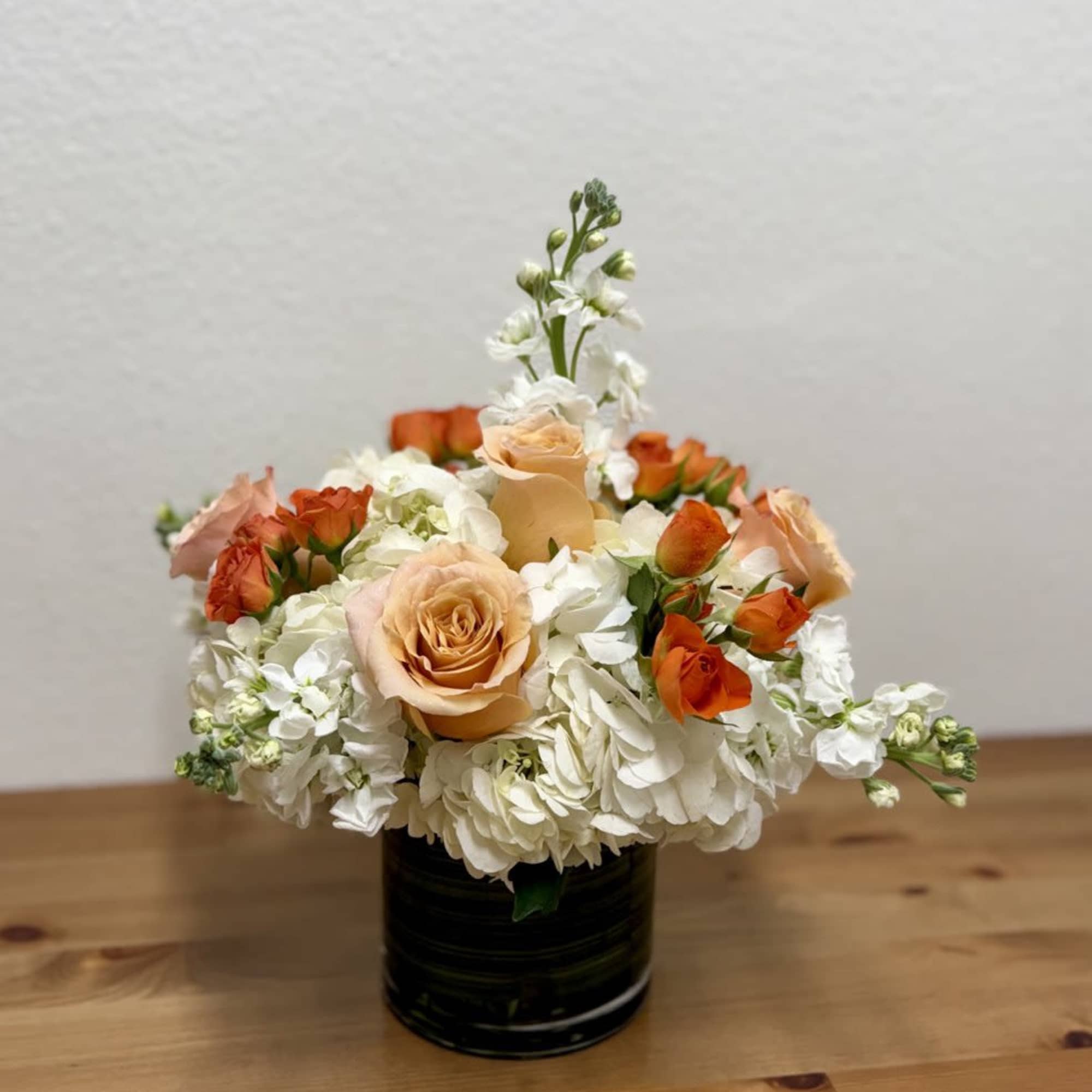 Peach roses and white flowers arranged in a black vase