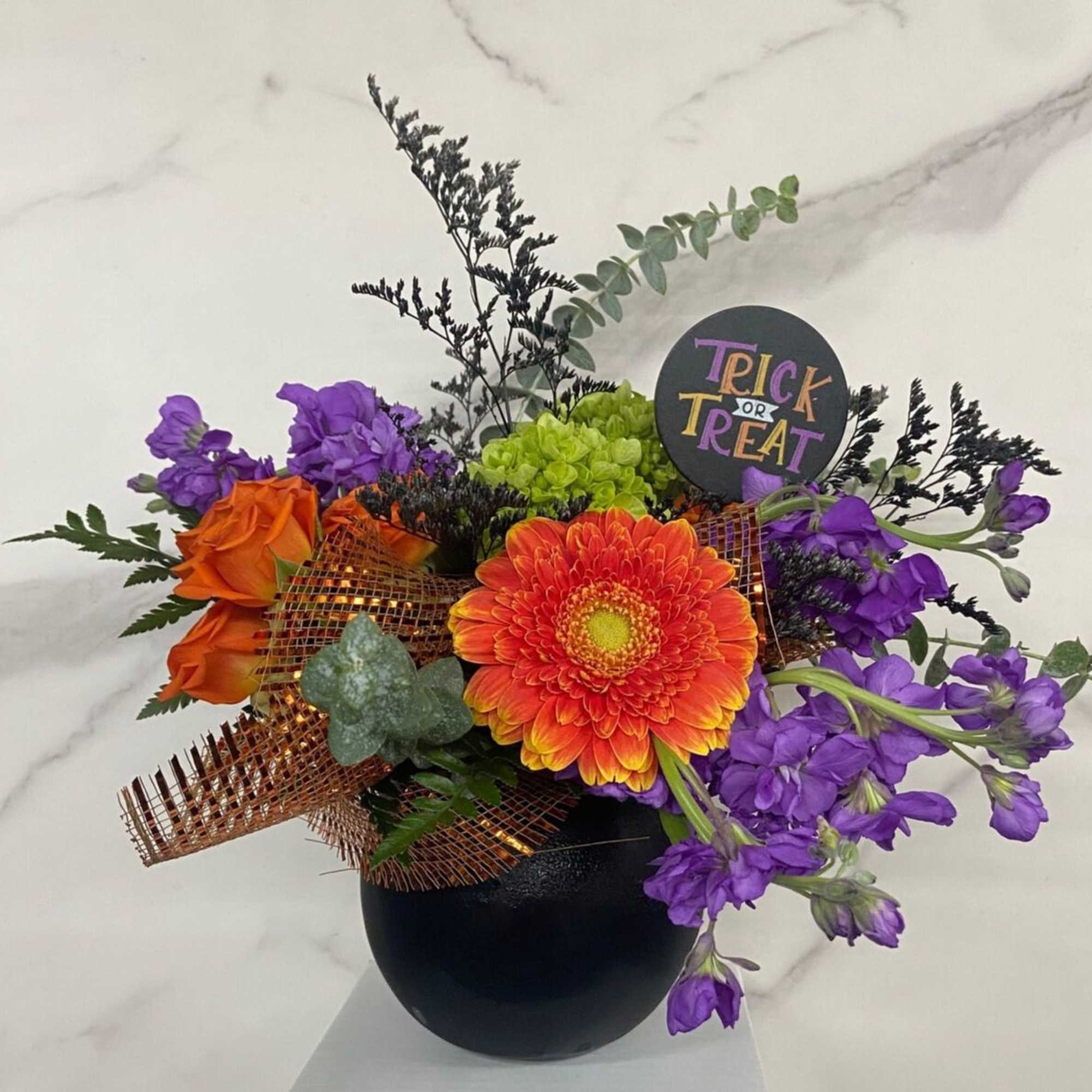 Orange and purple floral arrangement in a black vase with a Trick or Treat sign
