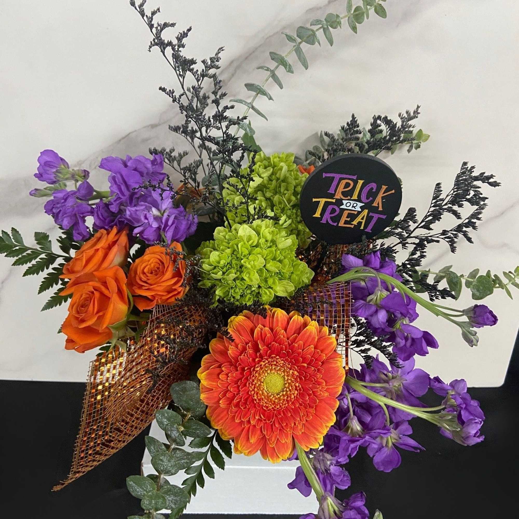Orange roses and a gerbera daisy with purple flowers in a box
