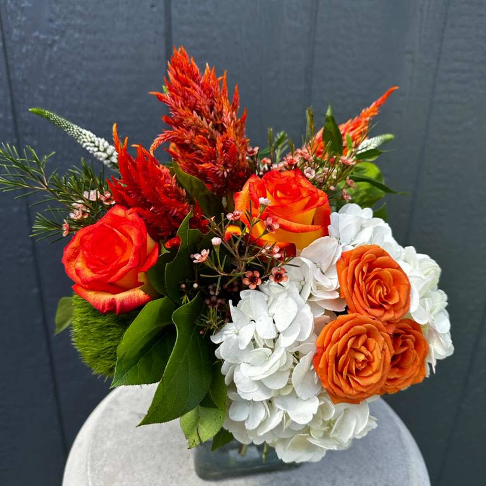 Orange roses and white hydrangeas in a glass vase with red plumes