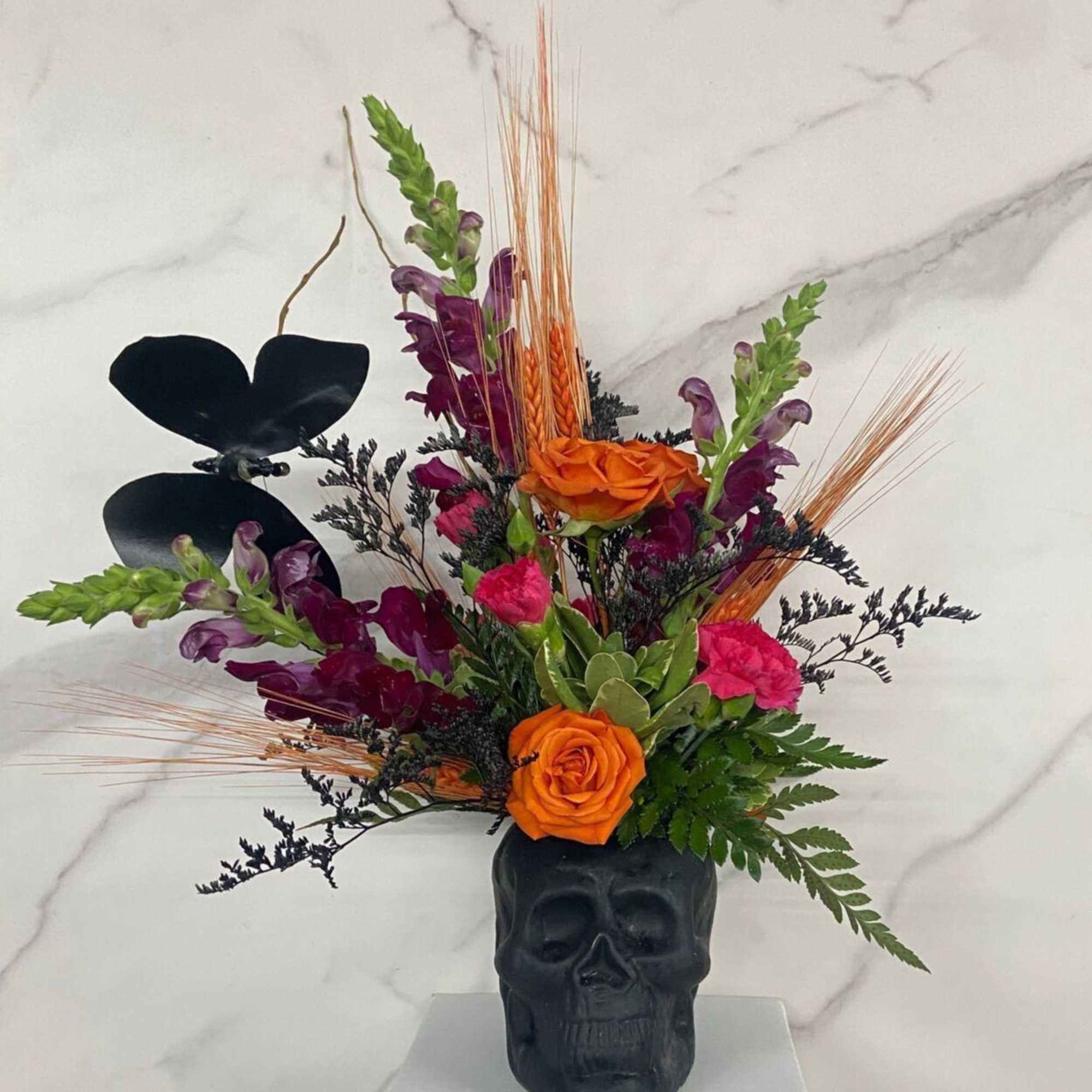 Orange and purple floral arrangement in a black skull vase